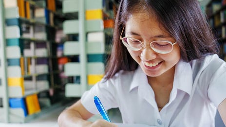 Niña sonriente escribiendo en su cuaderno mientras aprende italiano con Berlitz, en una biblioteca escolar
