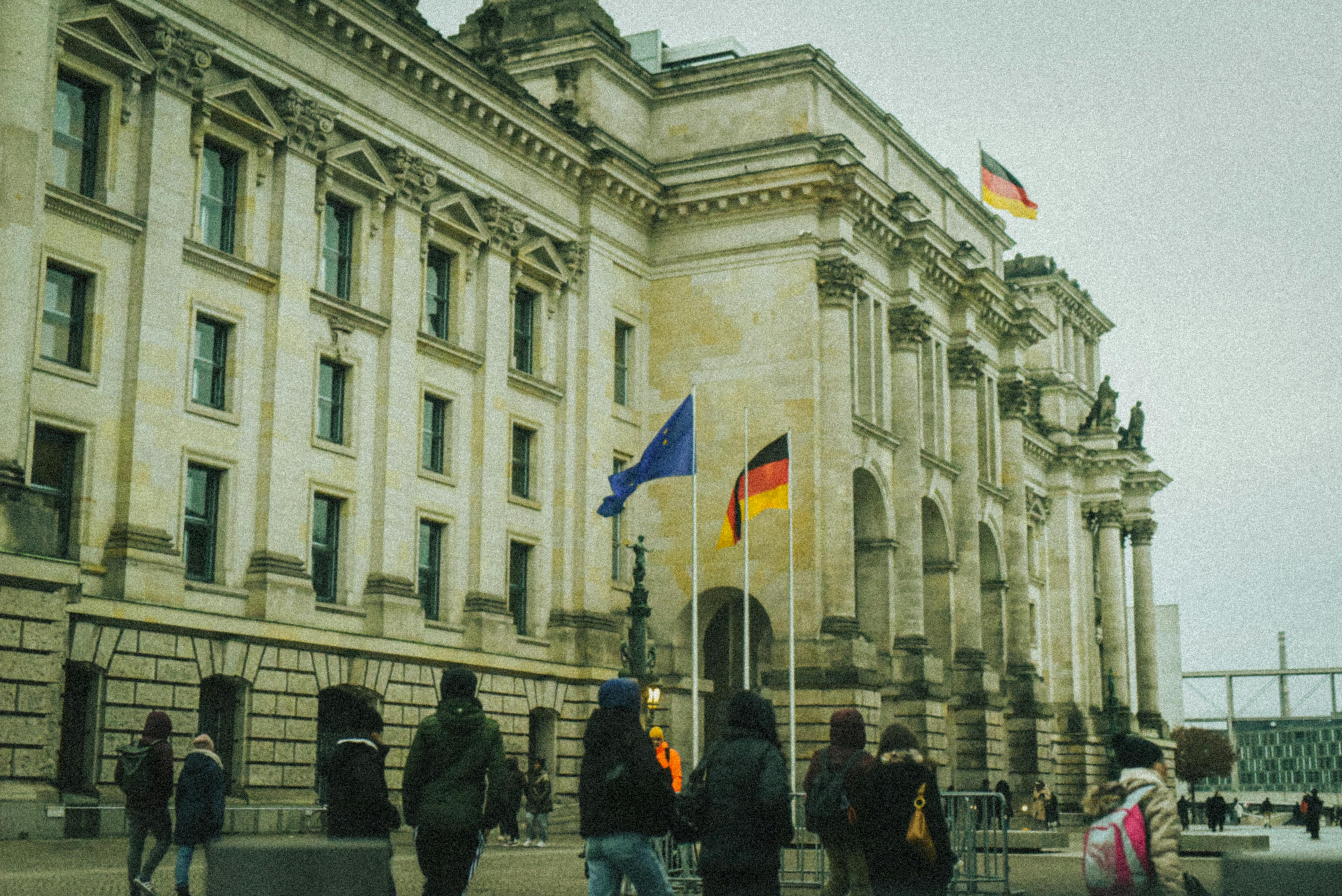 Varias personas caminan delante de un edificio con banderas alemanas.