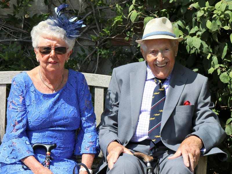 Una pareja de abuelos sentados en una banca de madera.
