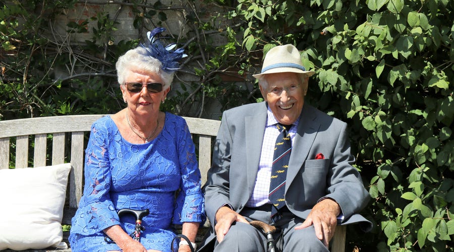 Una pareja de abuelos sentados en una banca de madera.