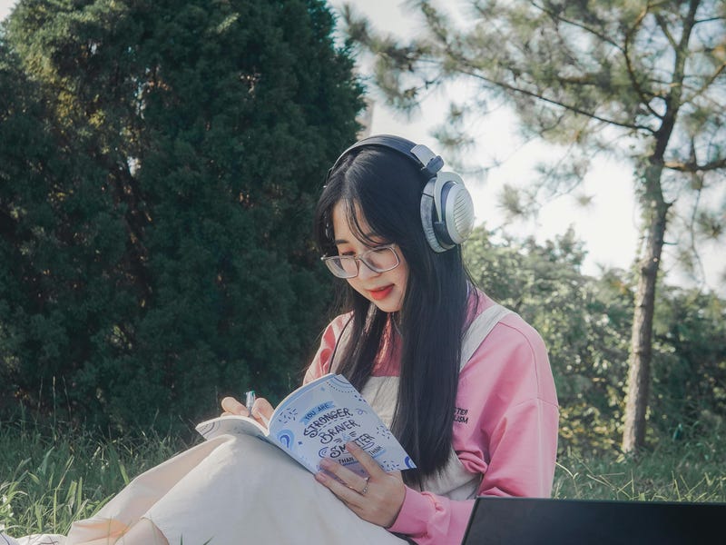 Chica estudiando al aire libre en un jardín para aprender portugués rápido.