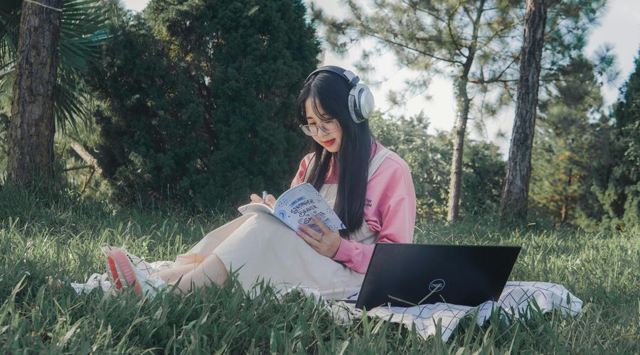 Chica estudiando al aire libre en un jardín para aprender portugués rápido.