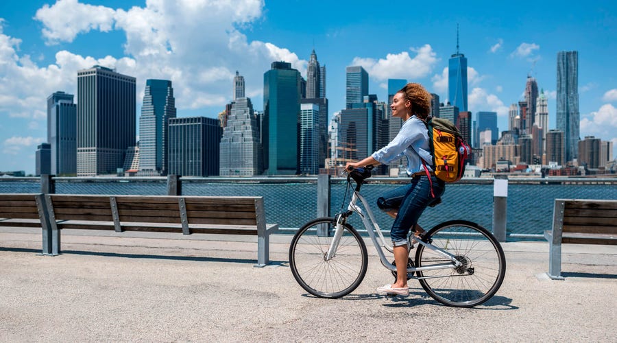 Mujer andando en bicicleta por Nueva York mientras estudia inglés con Berlitz, rodeada del skyline de Manhattan