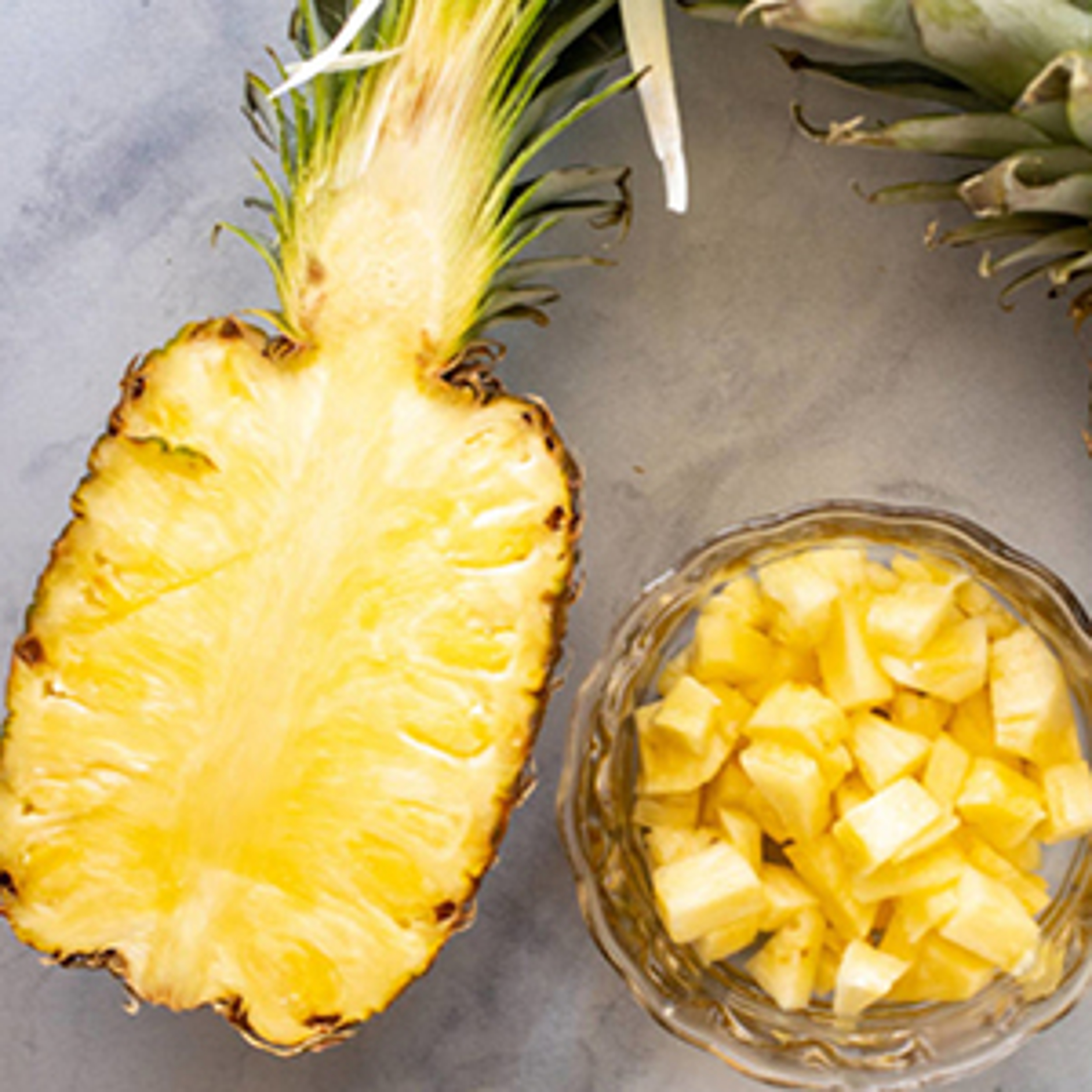 Pineapple sliced in half with a bowl of pineapple chunks next to it.
