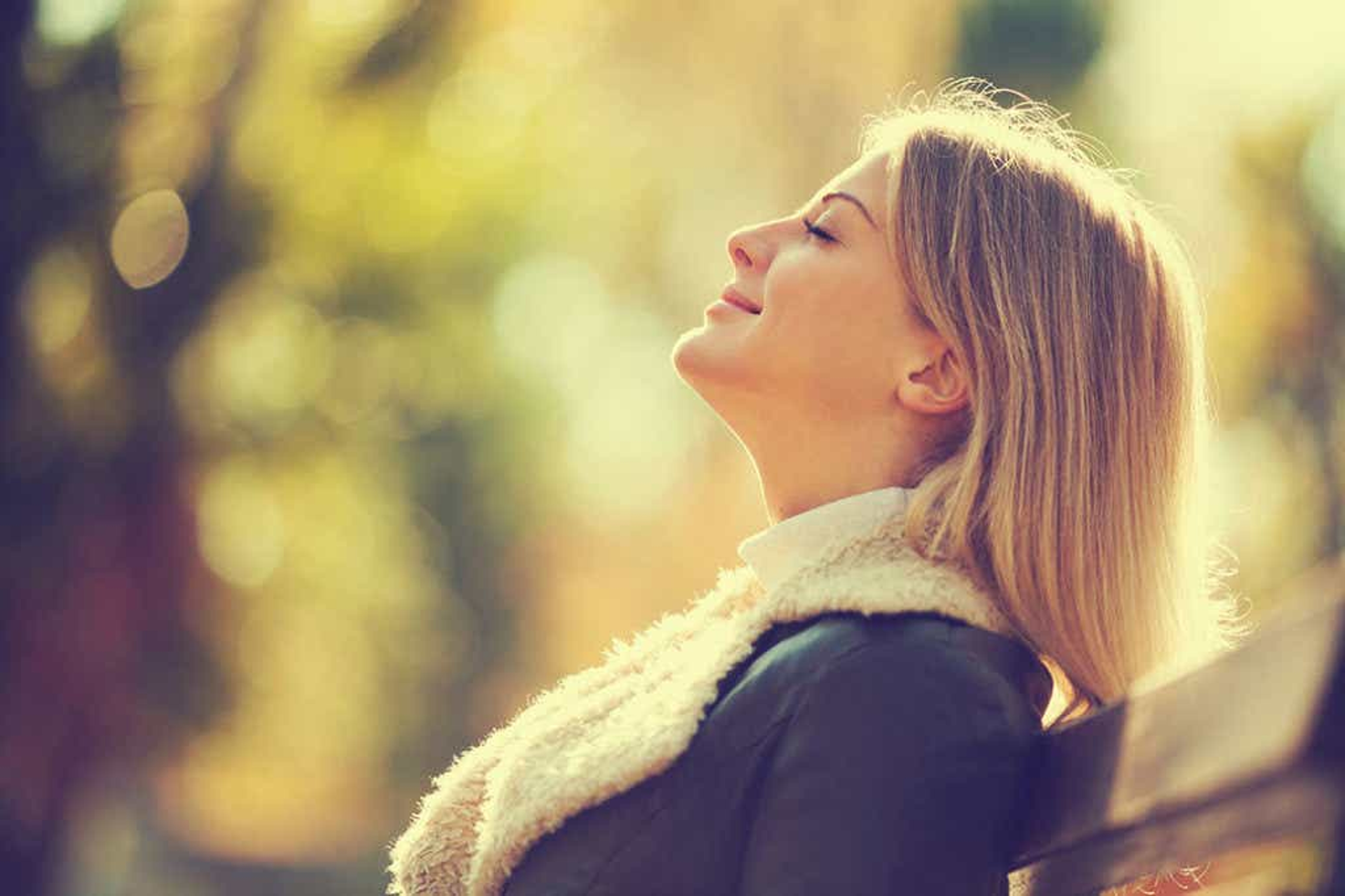 Women in the park wearing a jacket and scarf with her eyes closed