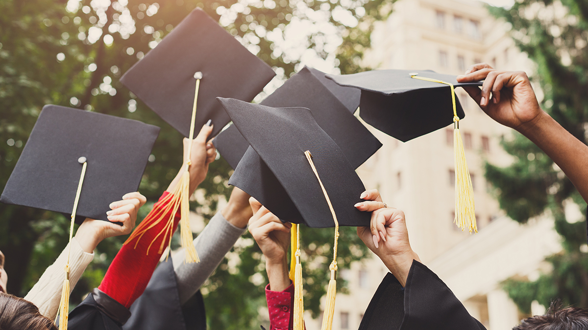 A group of multietnic students celebrating their graduation by throwing caps in the air closeup. Education, qualification and gown concept.