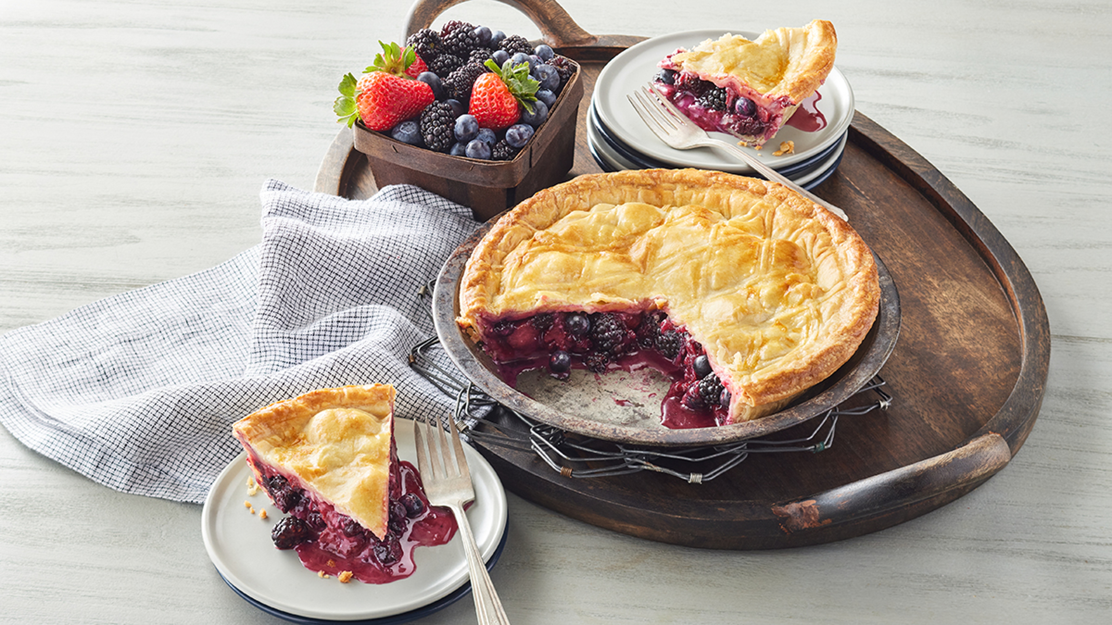 A berry pie on a platter with two slices on plates.