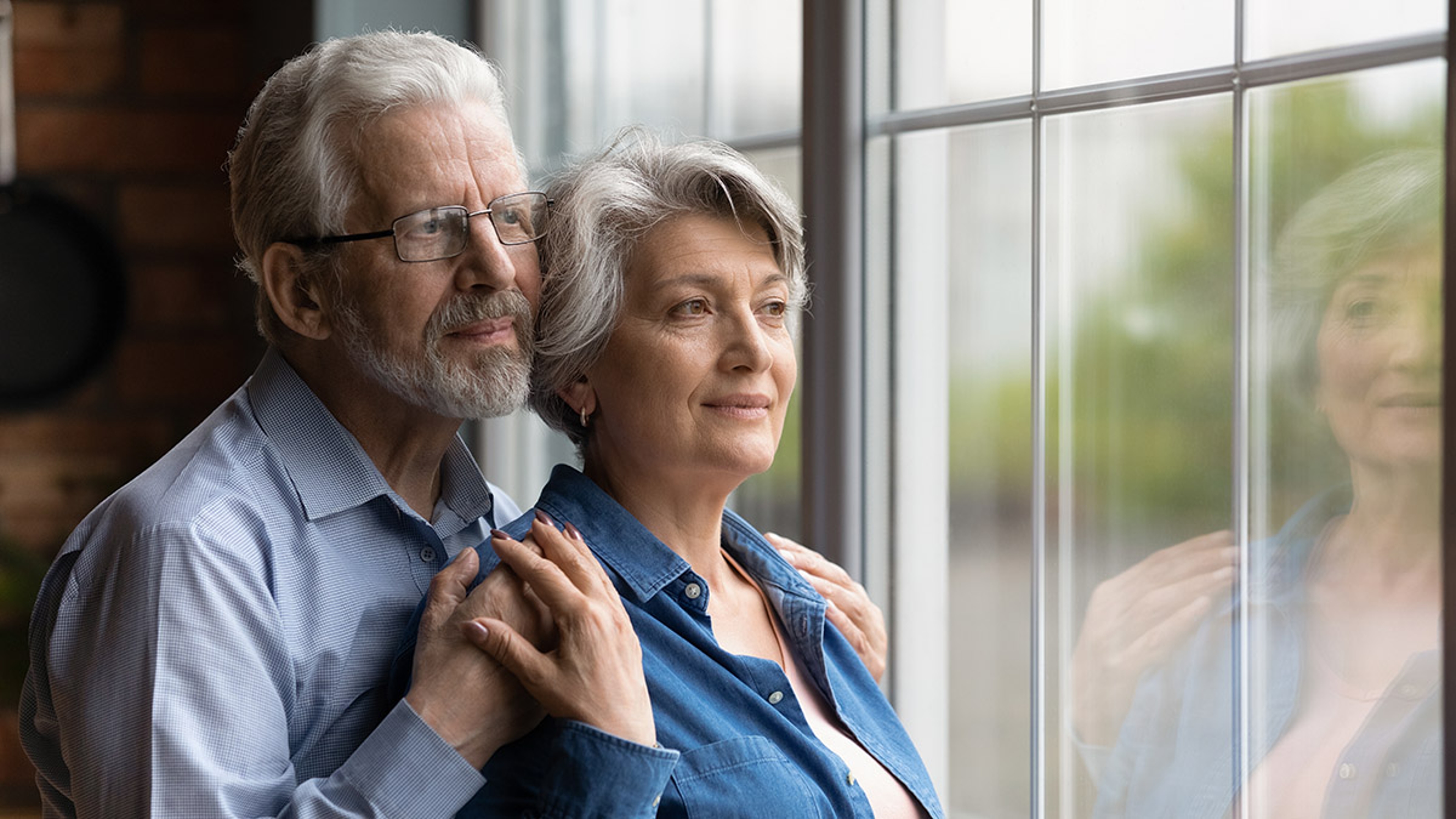Elderly spouses hug look at window meet twilight years together