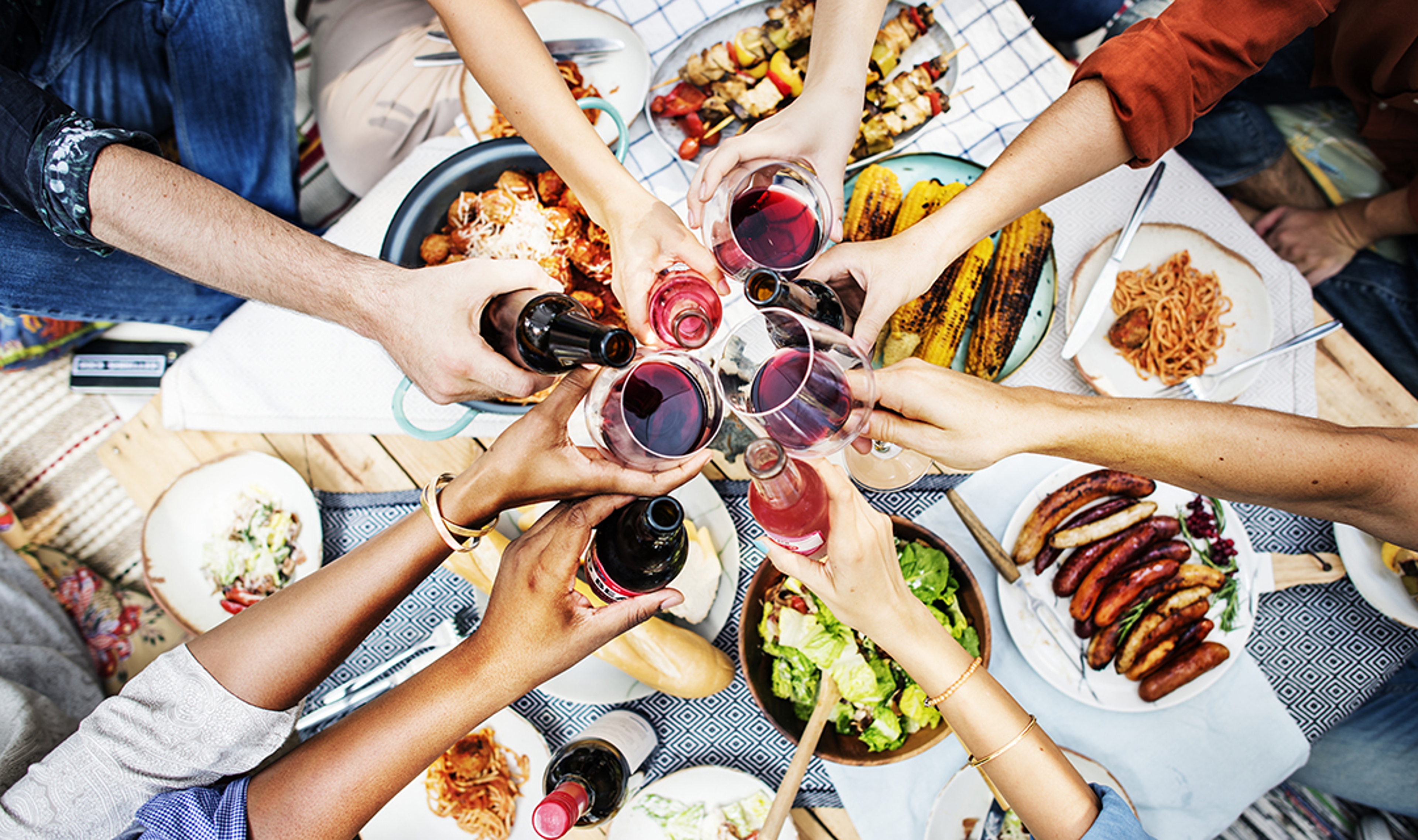 Overhead shot of people raising glasses of wine over a full table.
