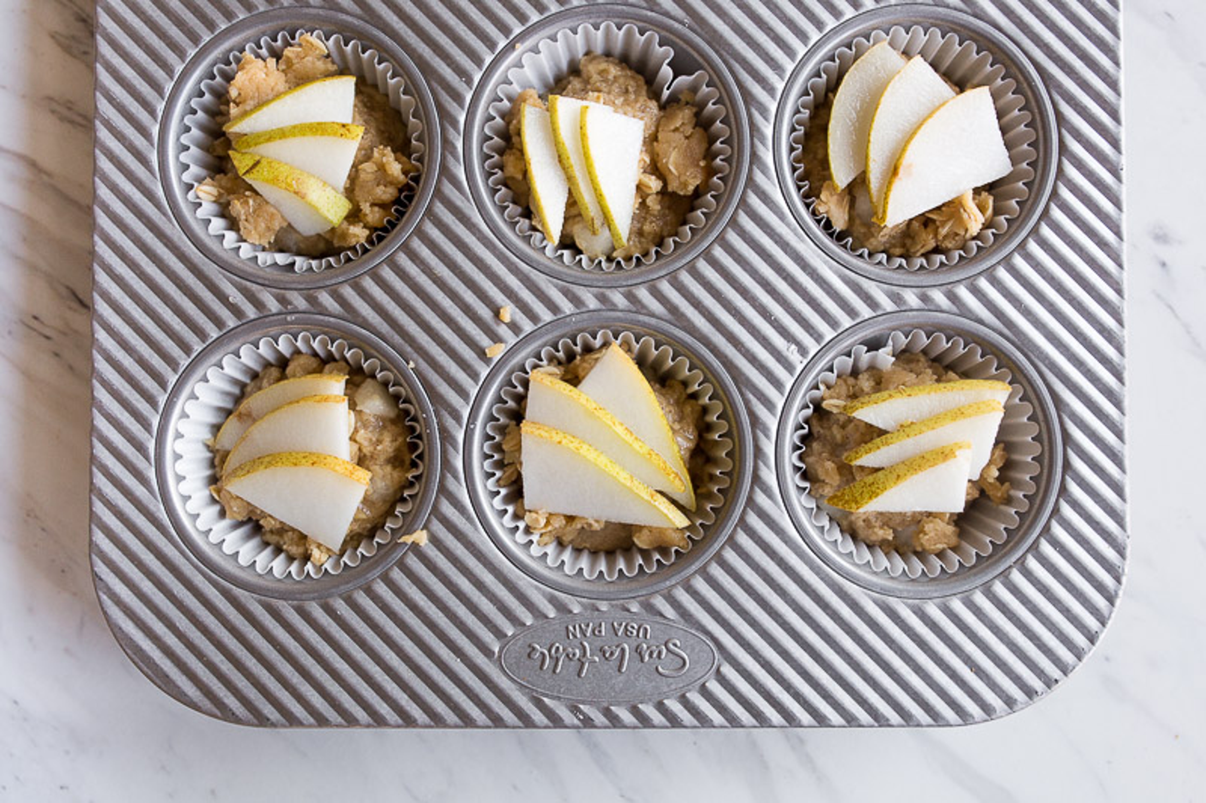 Pear muffins in a muffin tin topped with sliced pears.