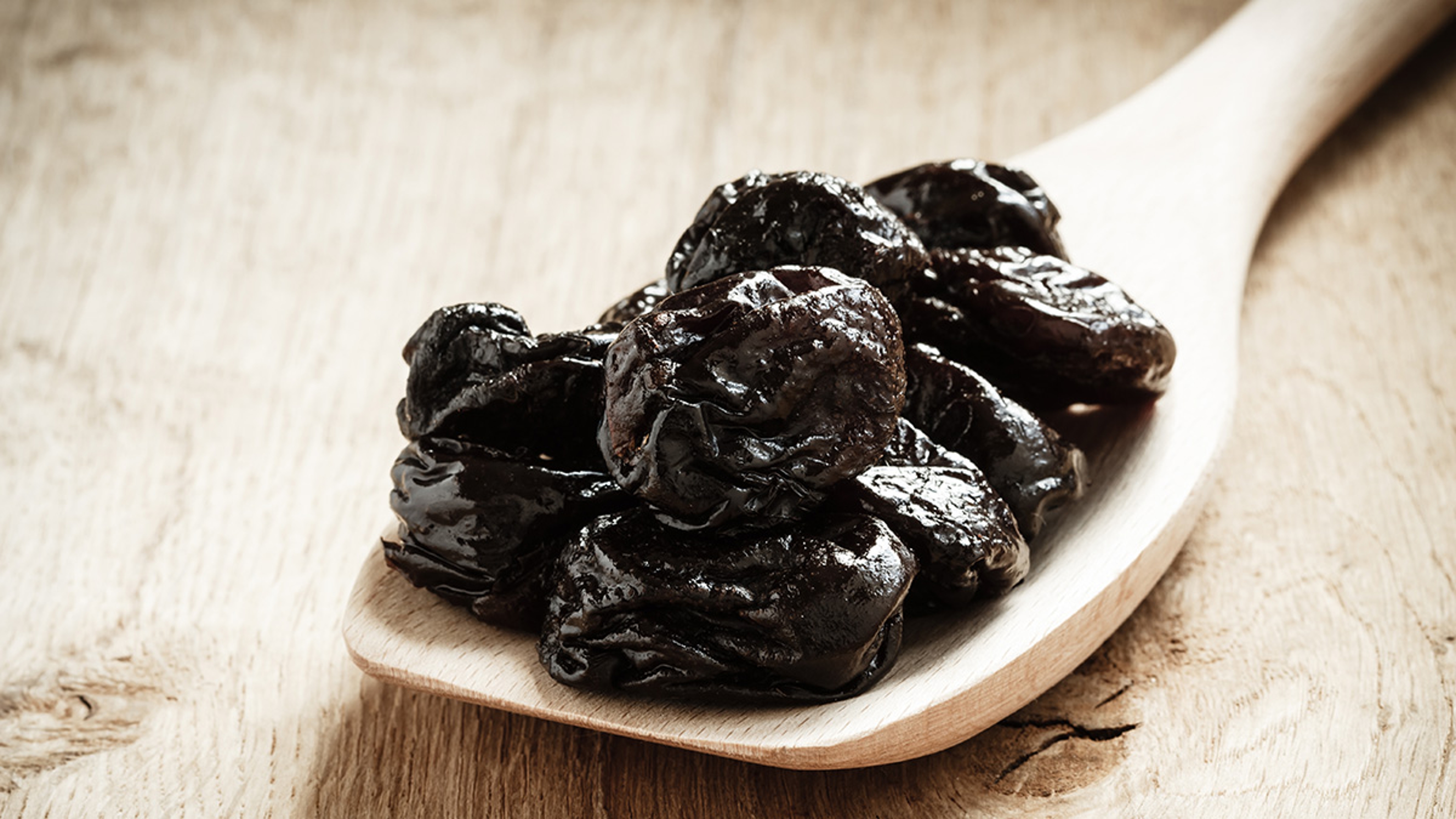 Healthy food, good cuisine. Closeup dried plums prunes fruits on wooden spoon rustic table background