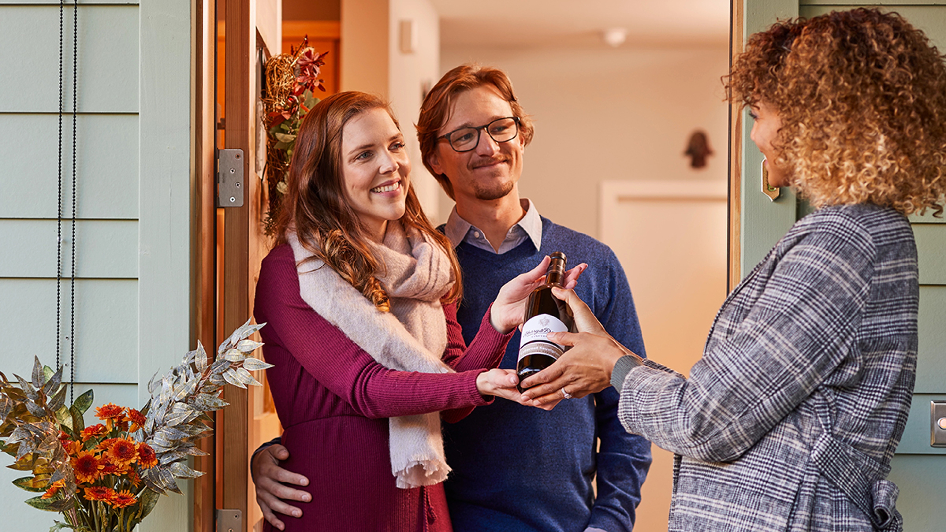 valentine's day gifts for couples woman handing a bottle of wine to a husband and wife at the front door