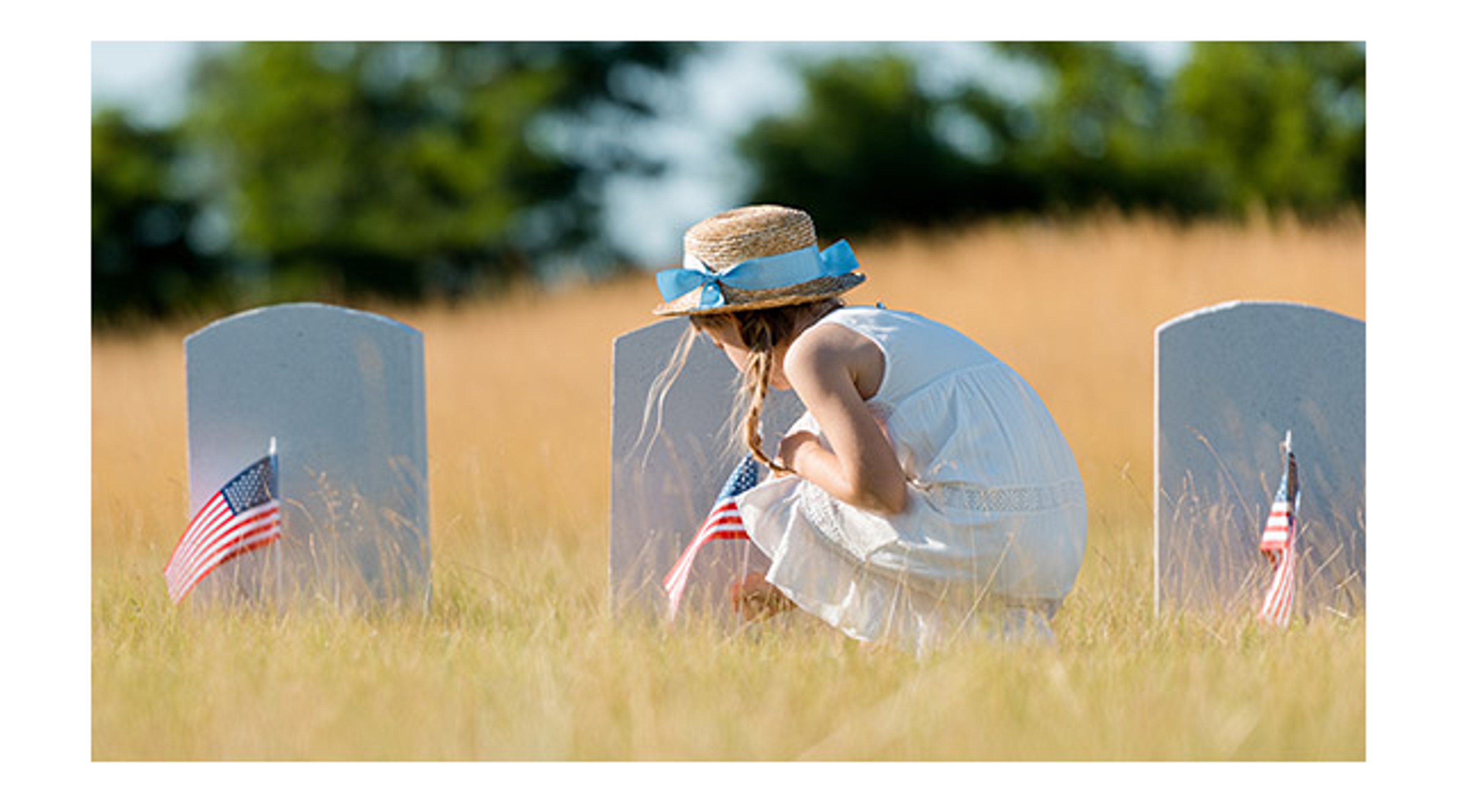 Photo of a little girl decorating a grave with flag for Memorial Day