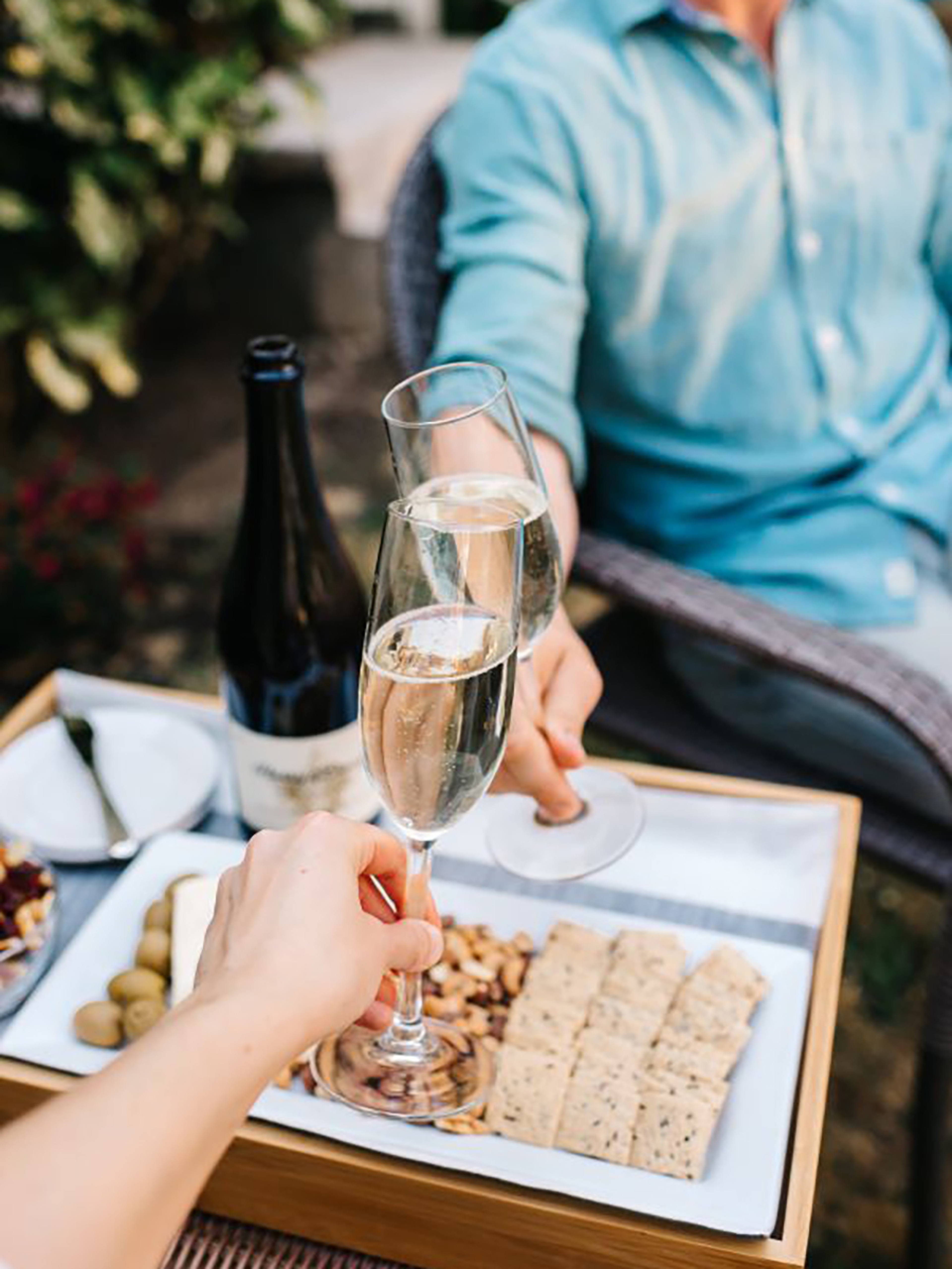 wine trends with two hands clinking glasses of sparkling wine over a spread of snacks and cheese.