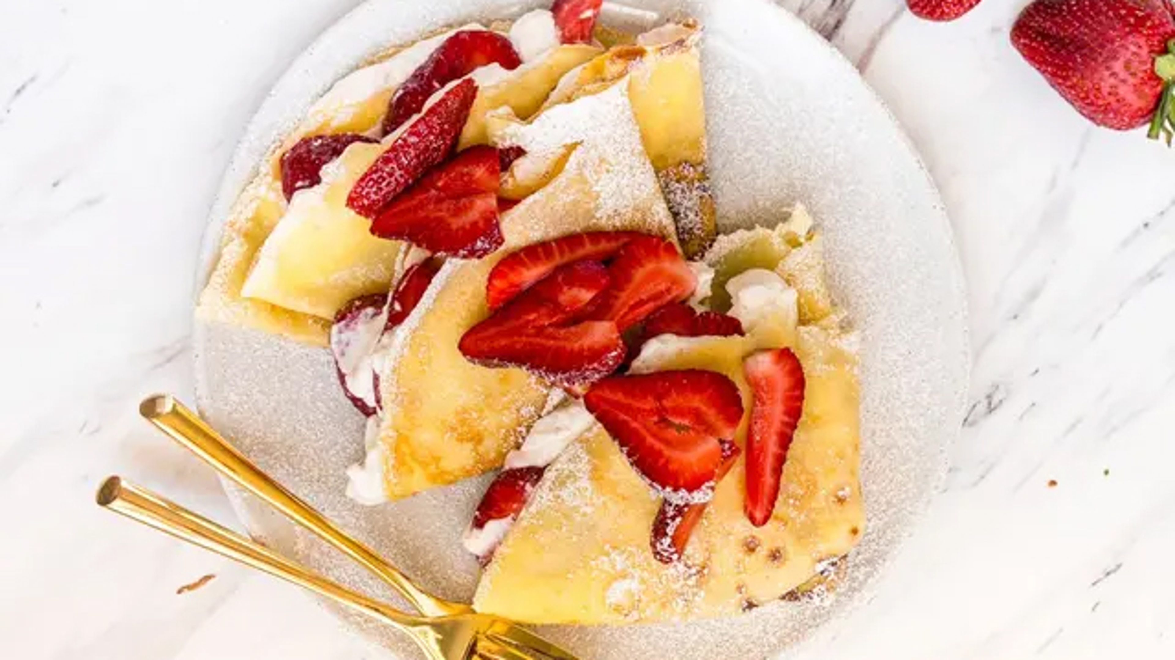 A plate of crepes topped with sliced strawberries.