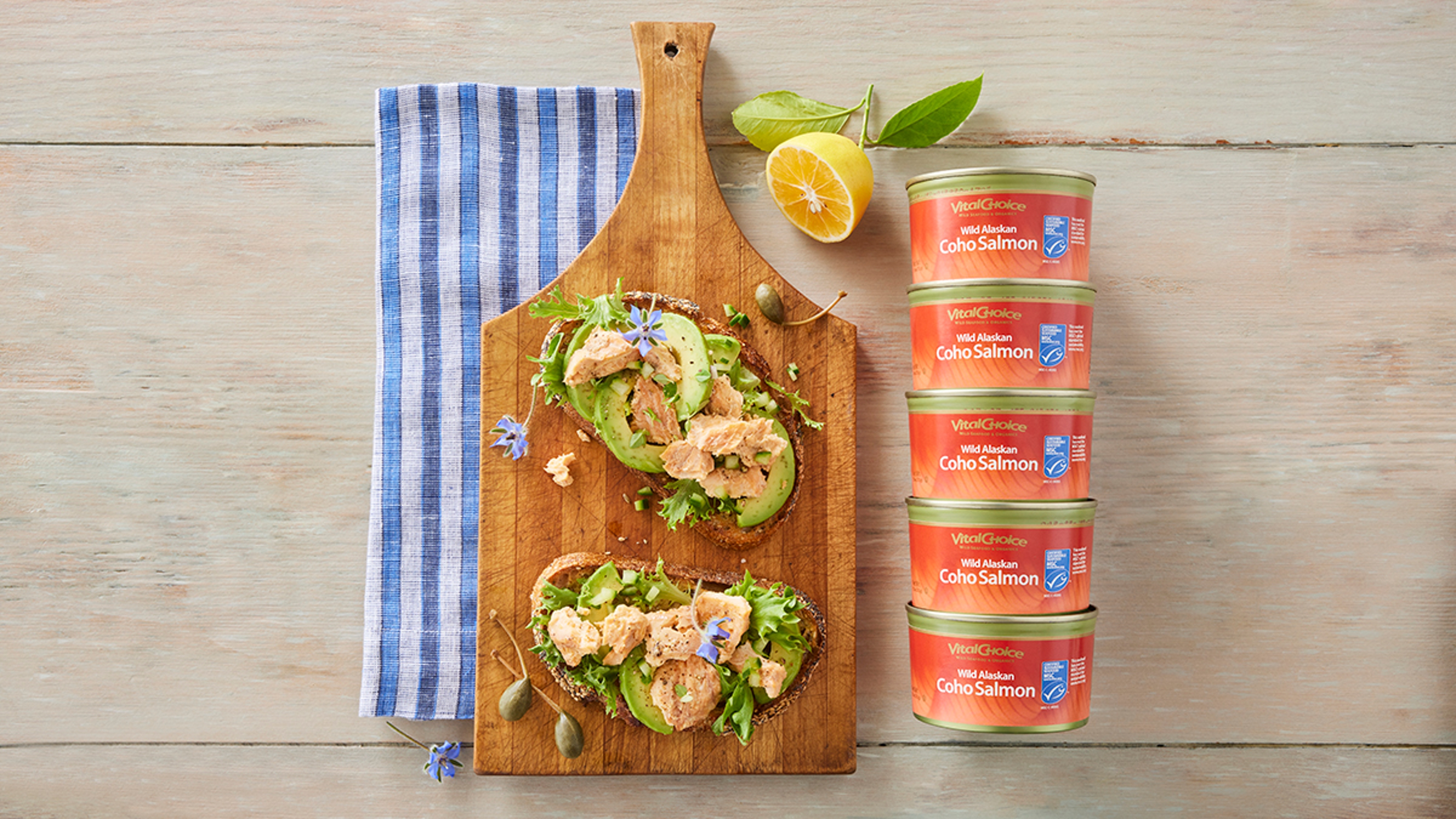 Tinned fish stacked on top of each other laying next to a cutting board with appetizers.