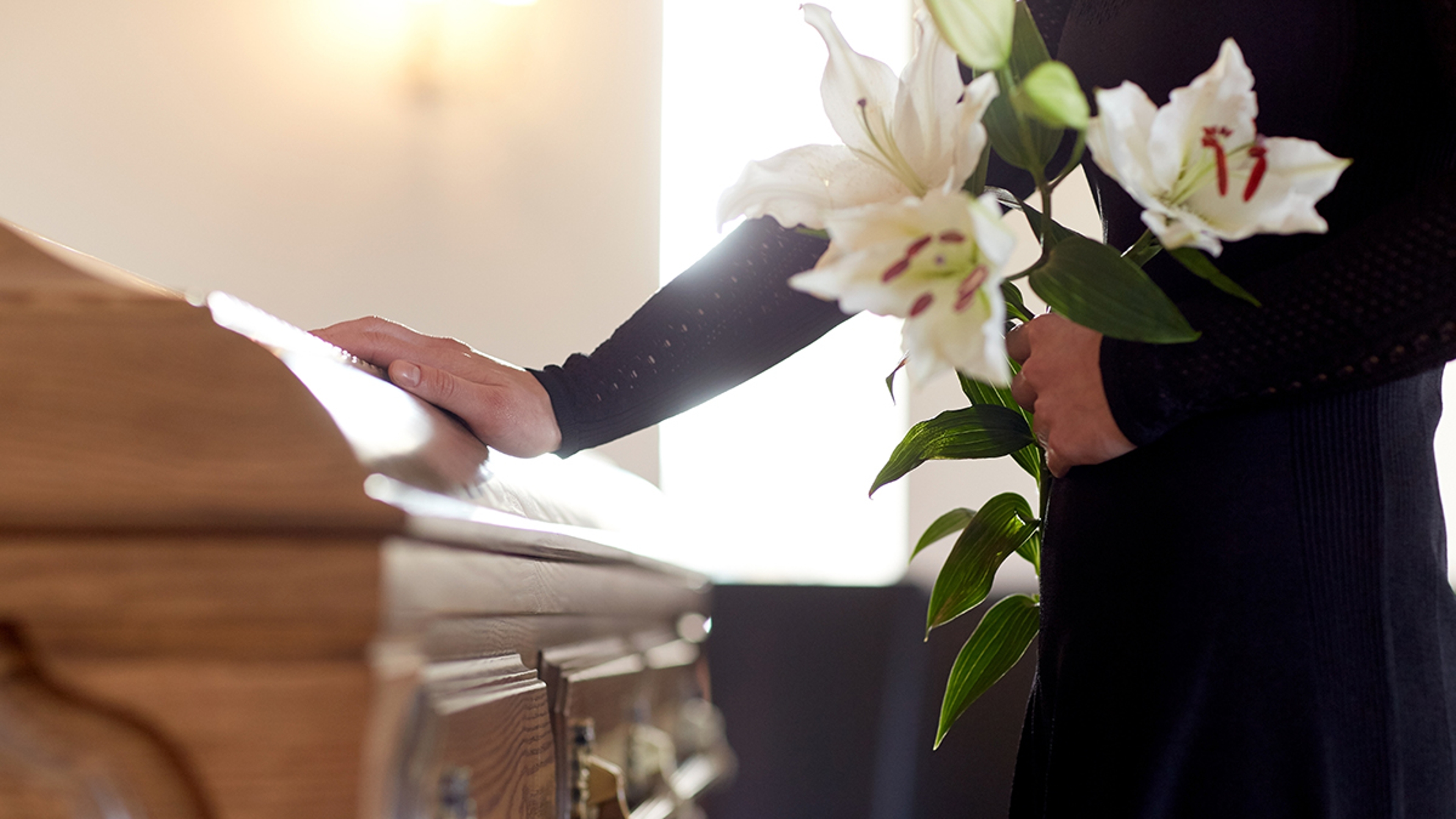 Someone holding lilies while touching a coffin.