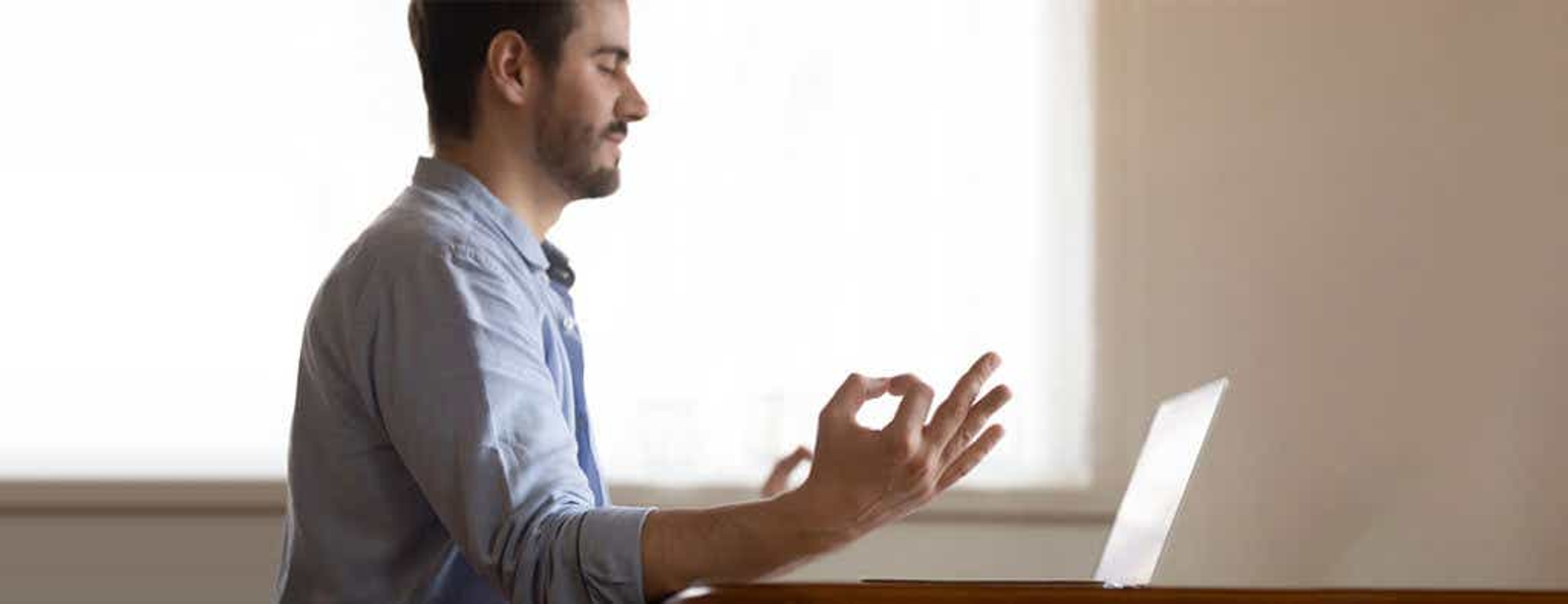 man sitting in a home office in front of his computer with eyes closed as he meditates