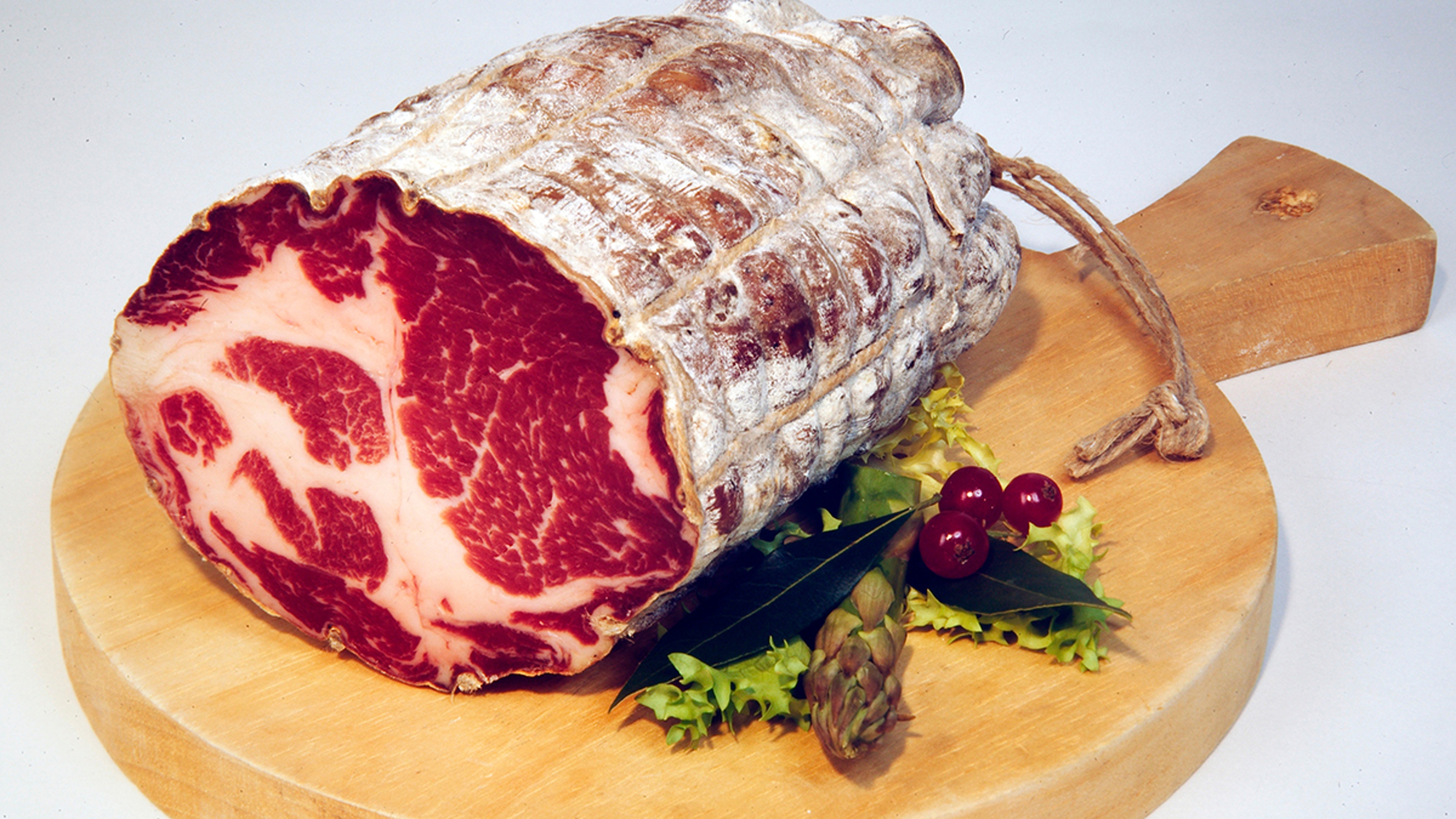 A photo of charcuterie with a cutting board holding a roll of salumi.