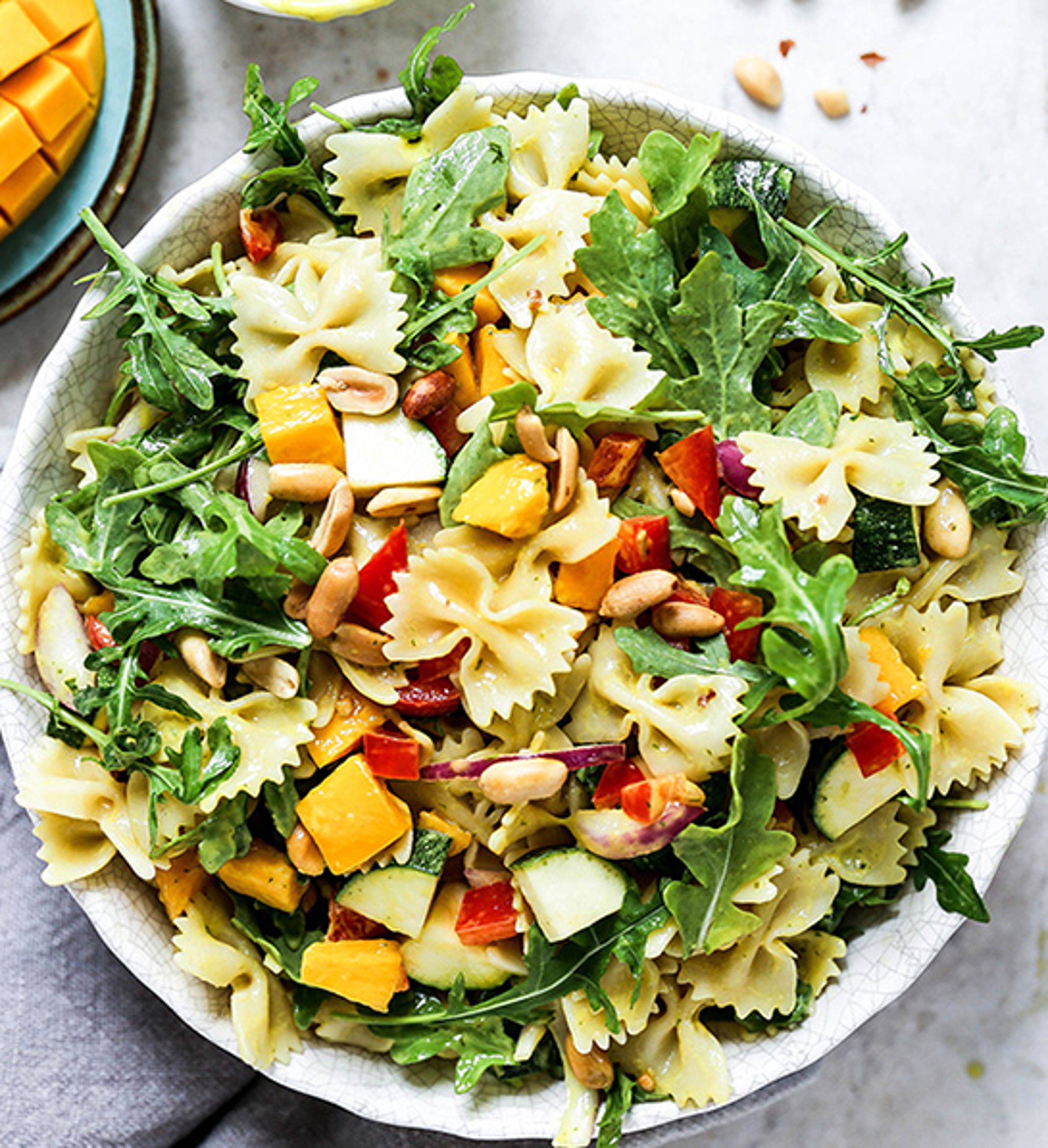 Bowl of pasta salad with mango and tomato slices.