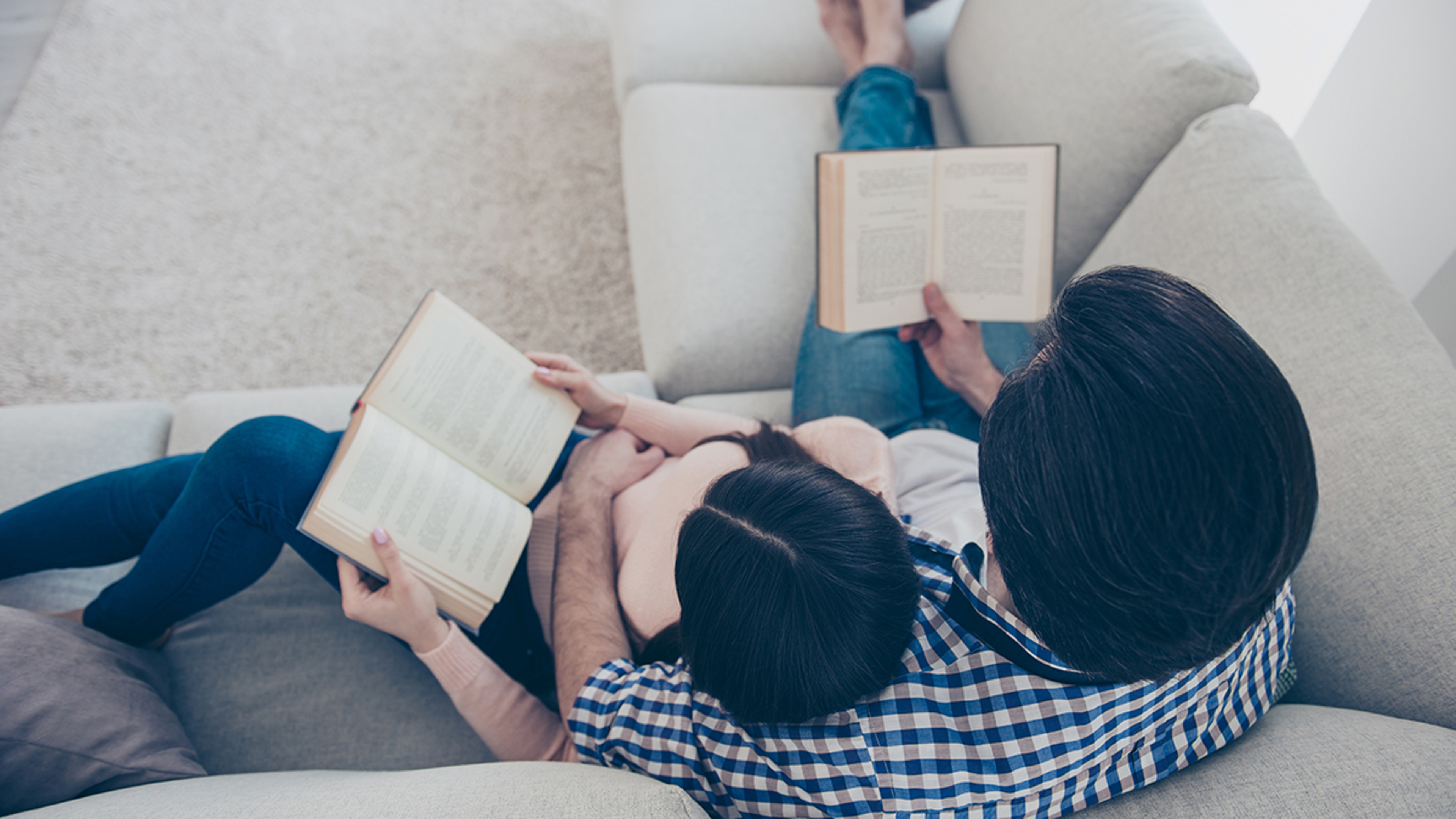 Article Cards Featured Image Top view portrait of well read lettered couple enjoying reading novel poem, poetry fans, lying on sofa having books in hands. Hobby free time self development education concept