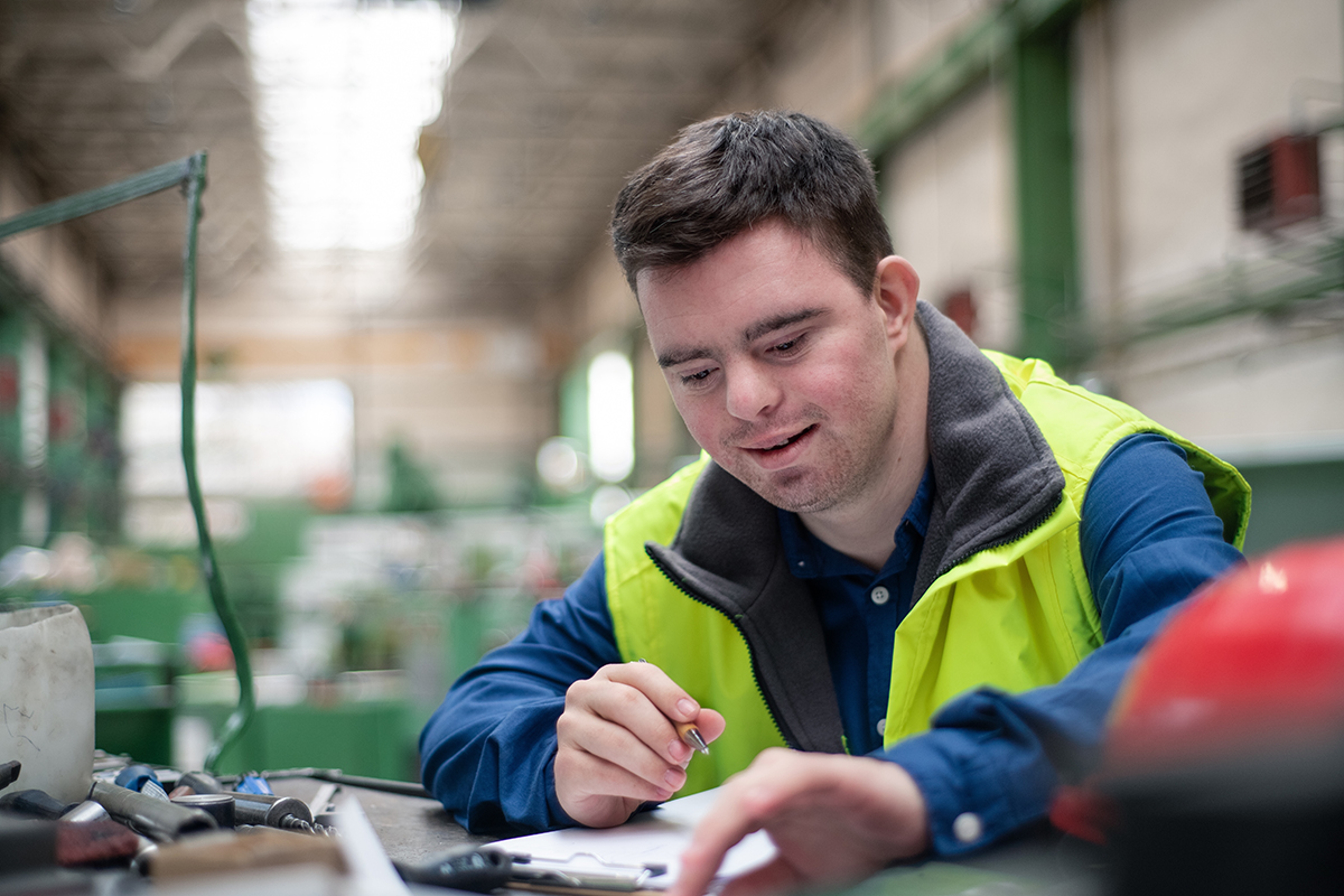 Article Cards Featured Image Young man with Down syndrome working in industrial factory, social integration concept.