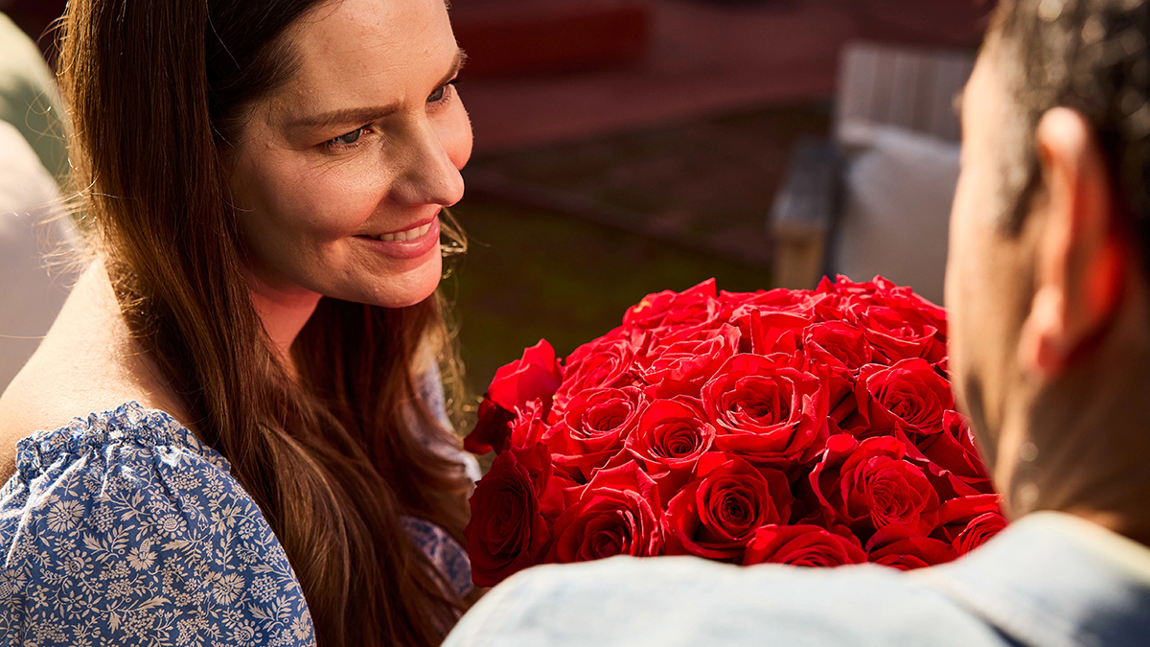 Woman holding a bouquet of red roses and smiling.