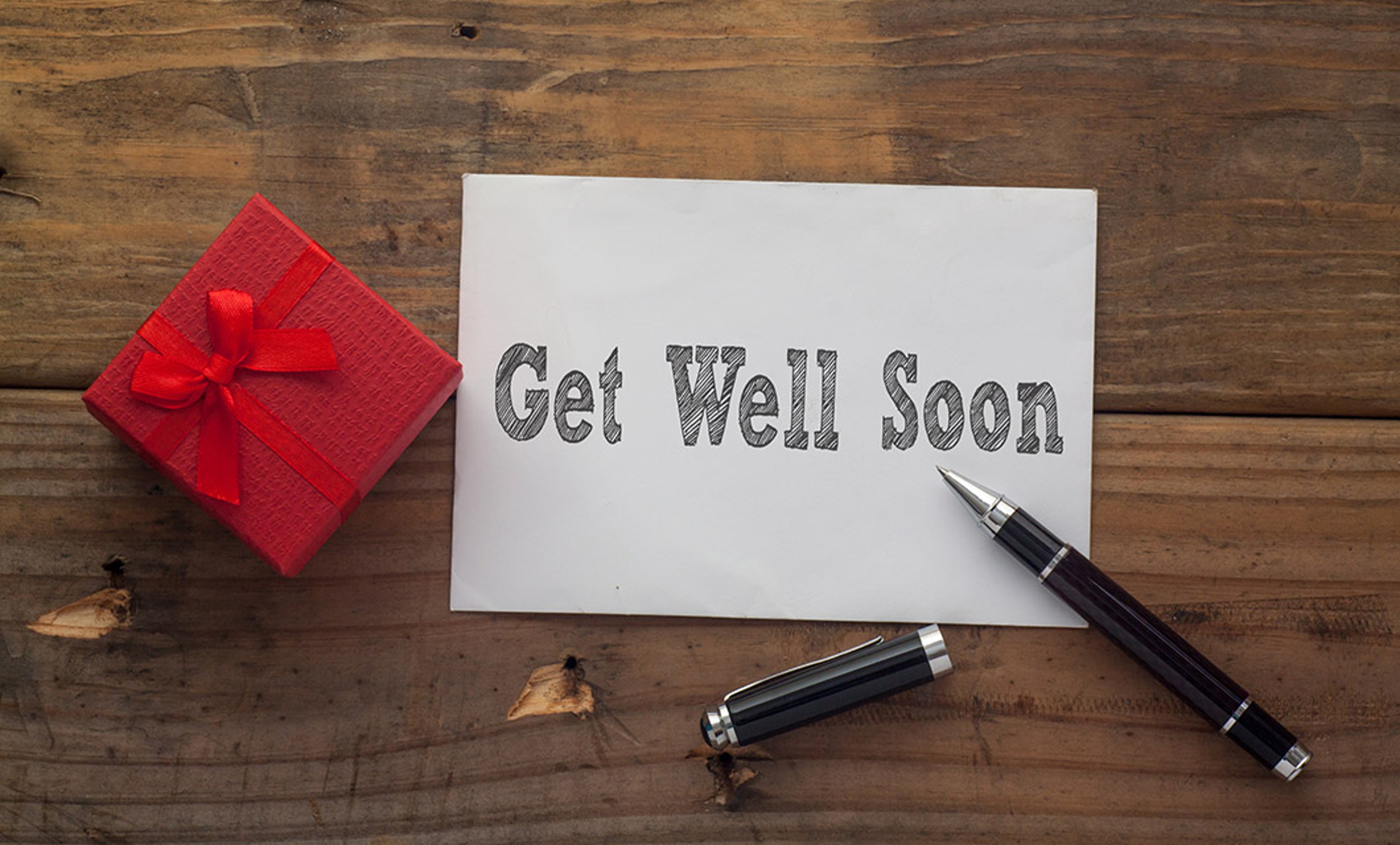 Article Cards Featured Image Get Well Soon written on paper with pen,red gift box and wooden background desk.