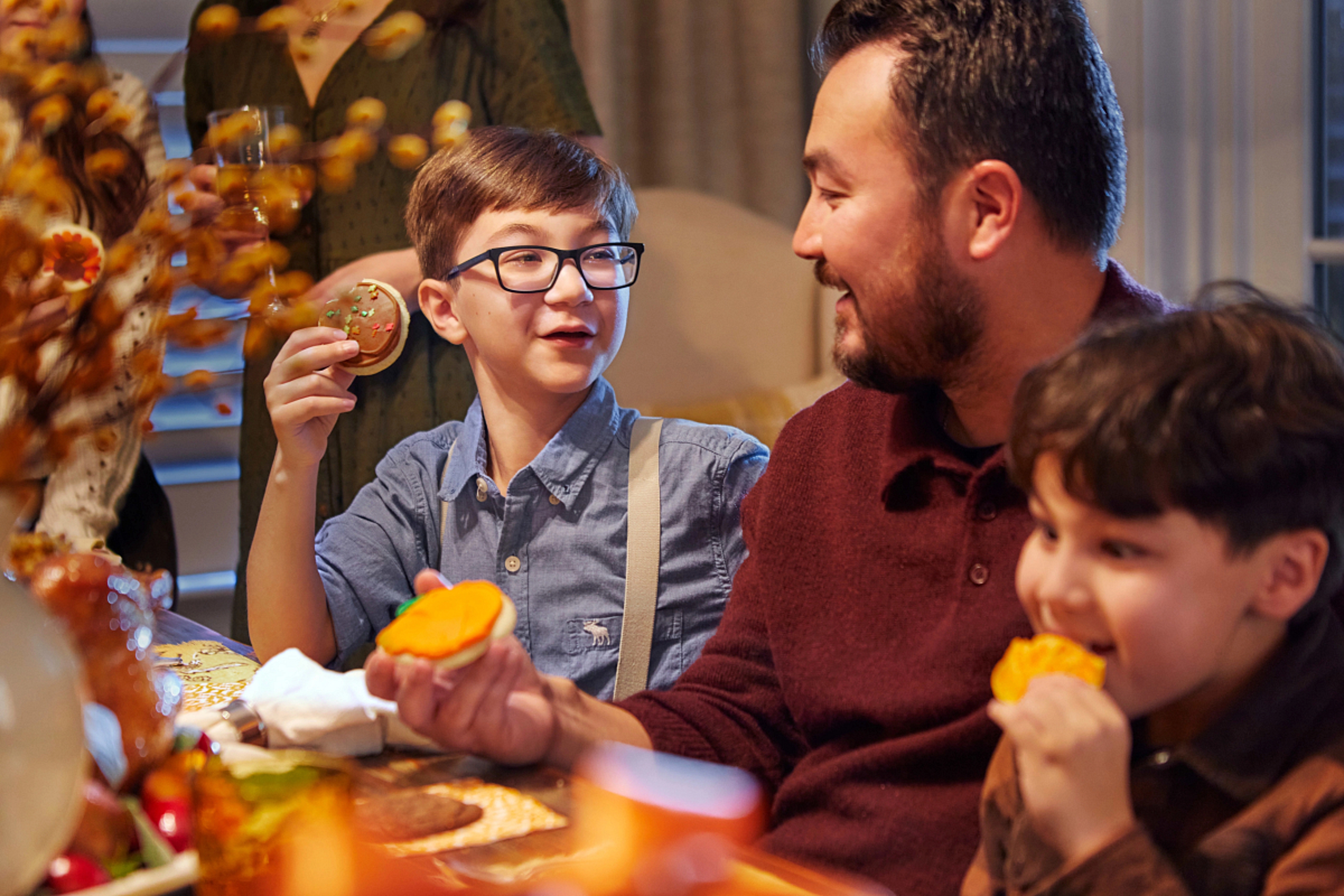 Sons and father expressing gratitude with cookies at a Thanksgiving table.