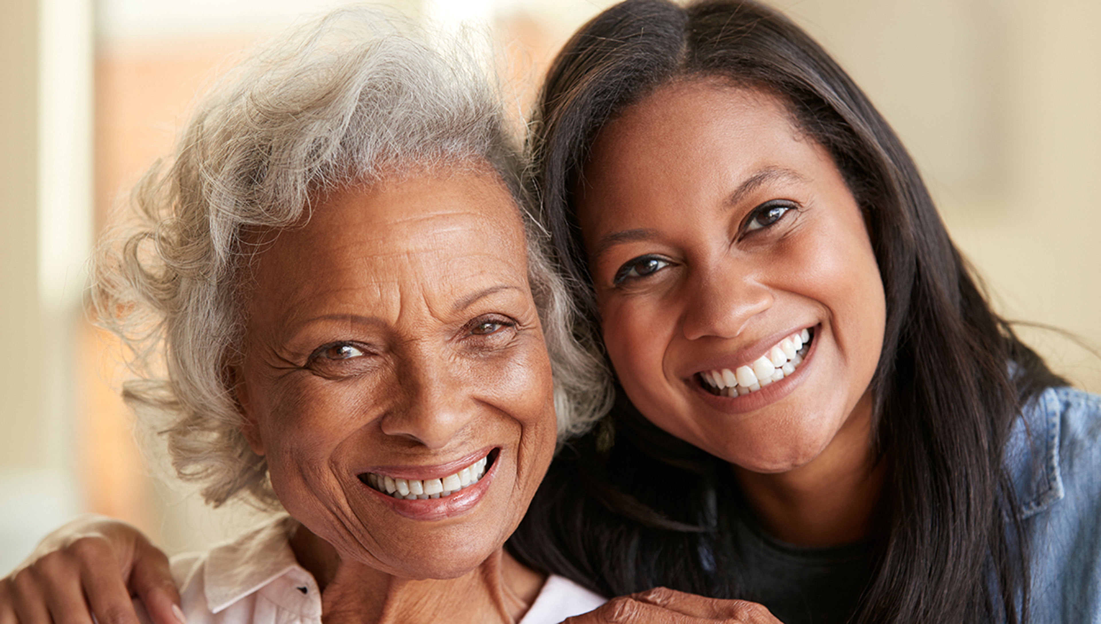 Portrait Of Senior Mother Being Hugged By Adult Daughter At Home