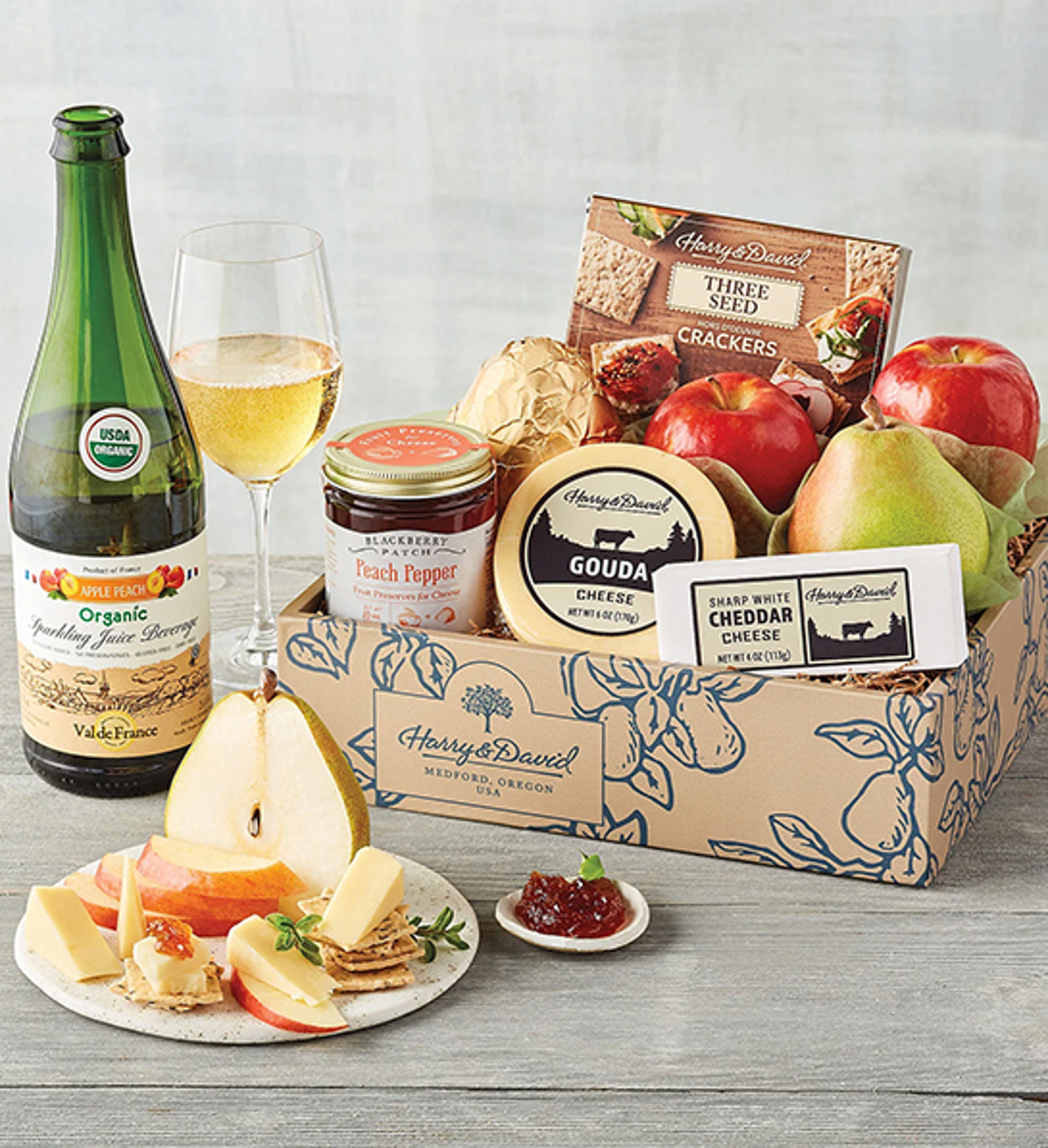 Box of fruit and cheese next to a bottle of sparkling cider.