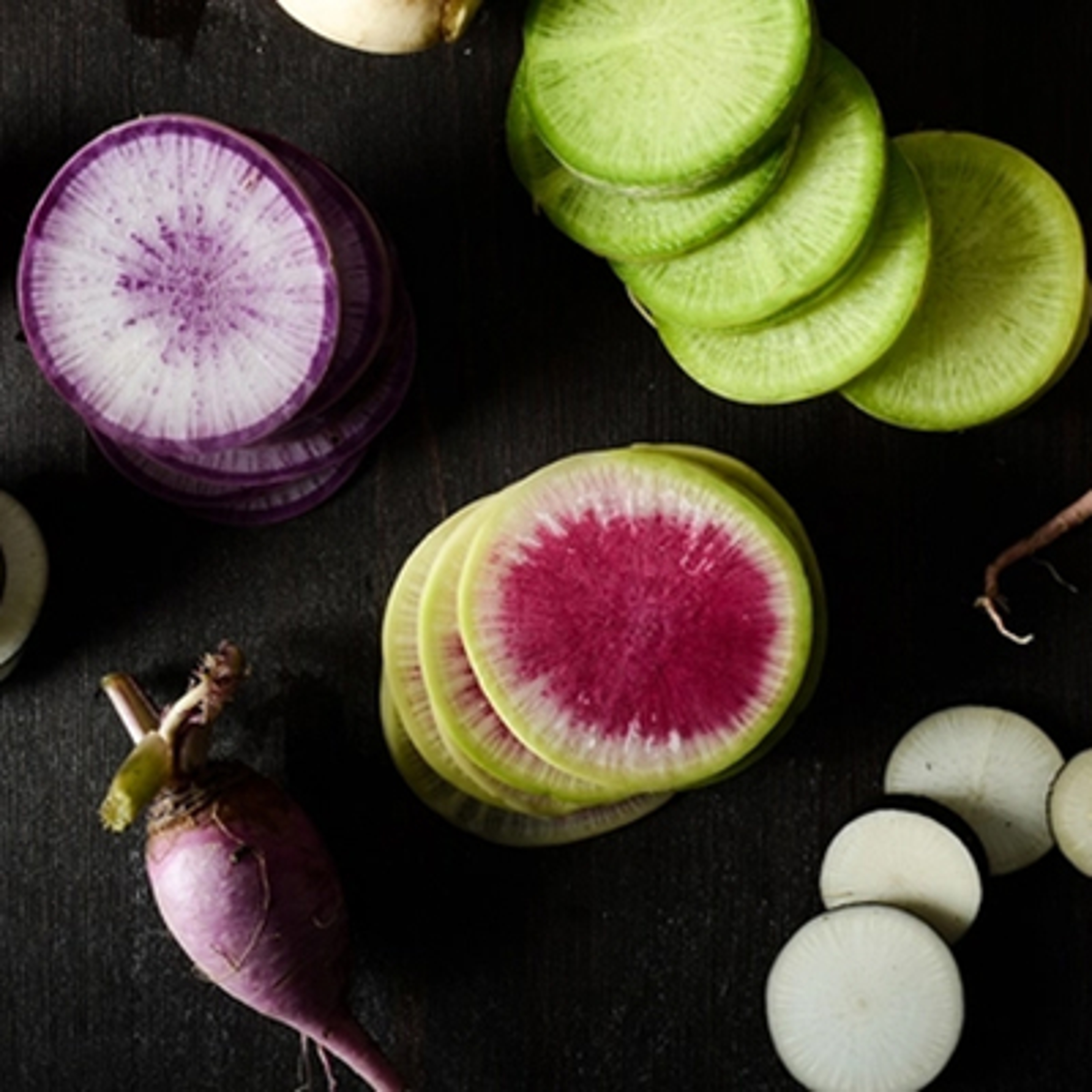 Types of radishes sliced and stacked on a black table.