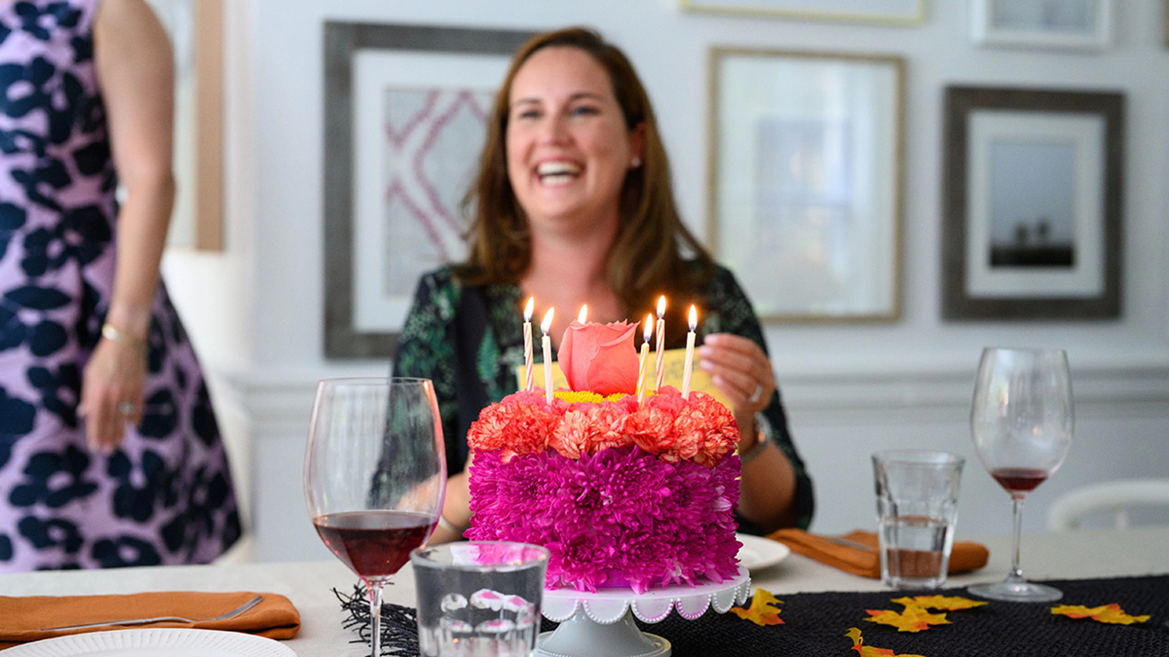 Flower cake for birthday with a woman sitting in the background smiling.