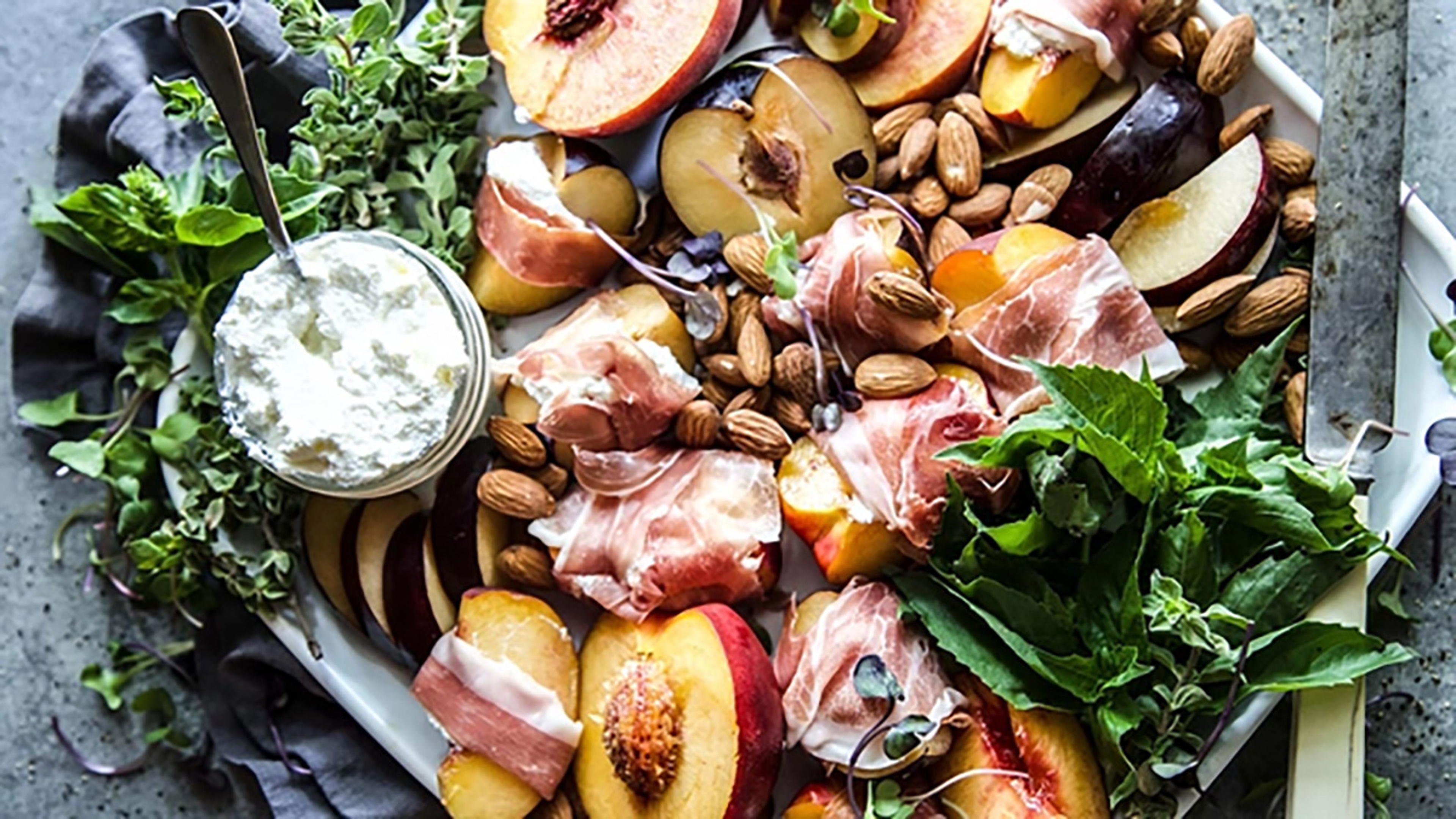 Peaches and plums wrapped in prosciutto on a platter.