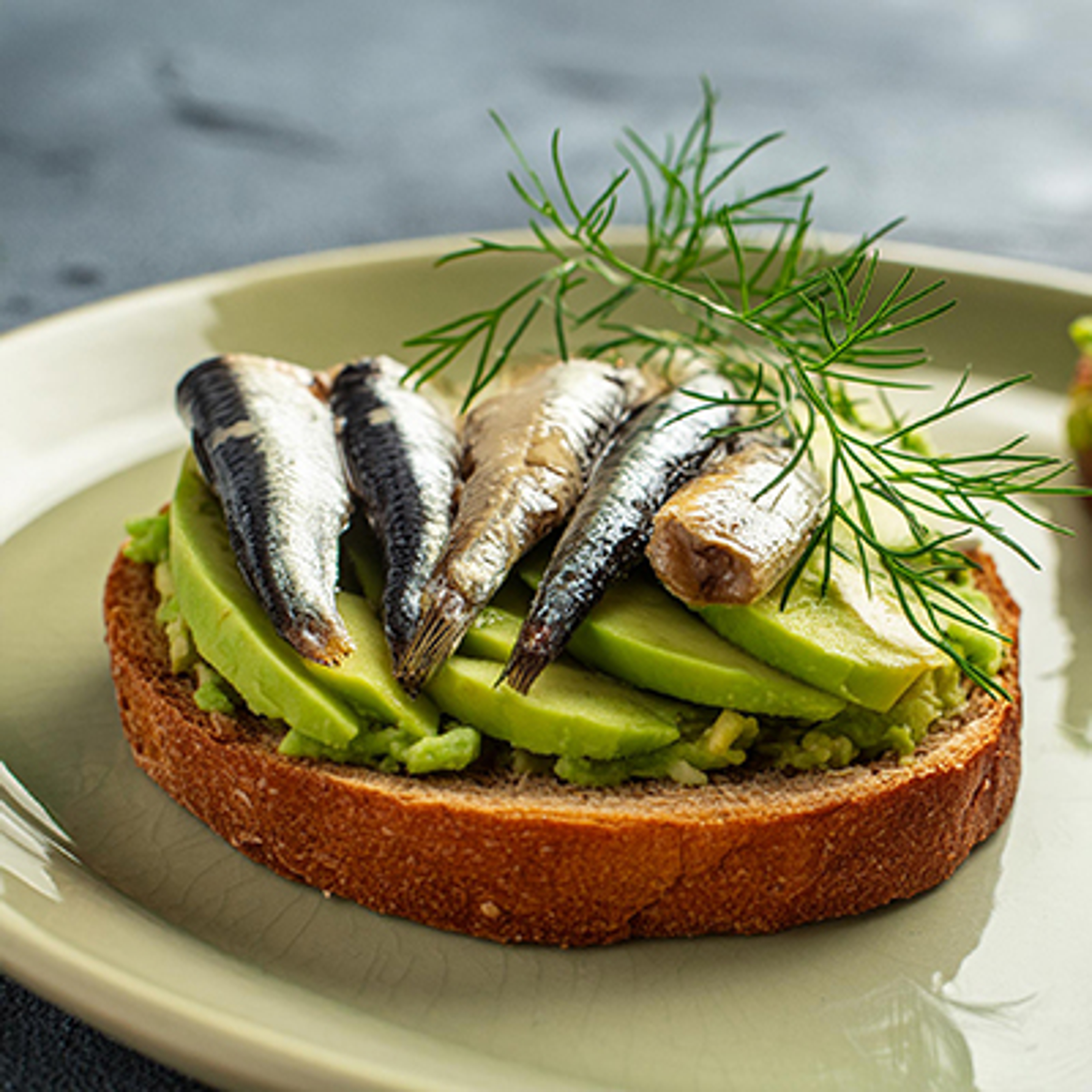 Smashed avocado toast topped with sardines and dill