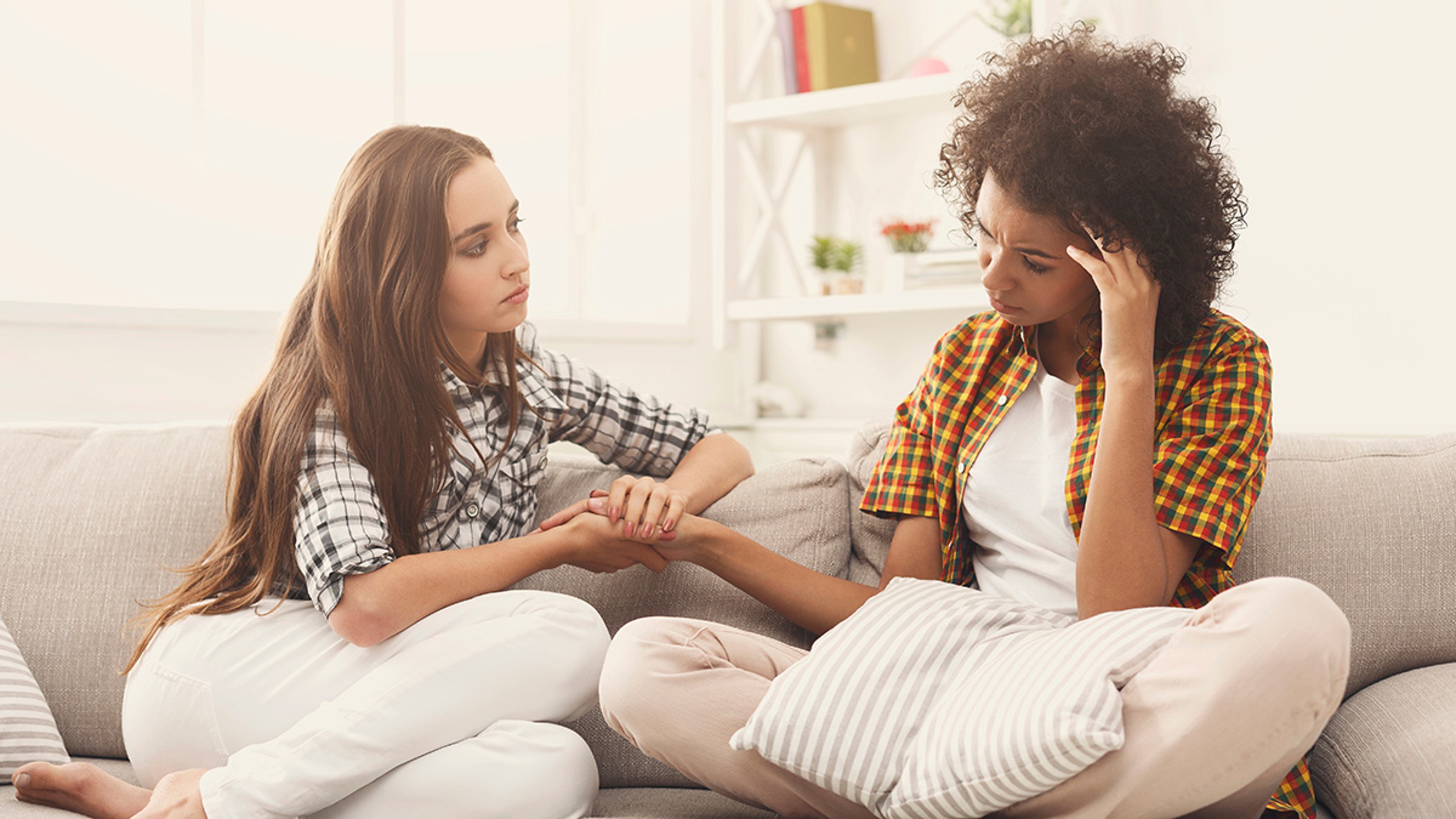 Two women sitting on a couch. One comforting the other.