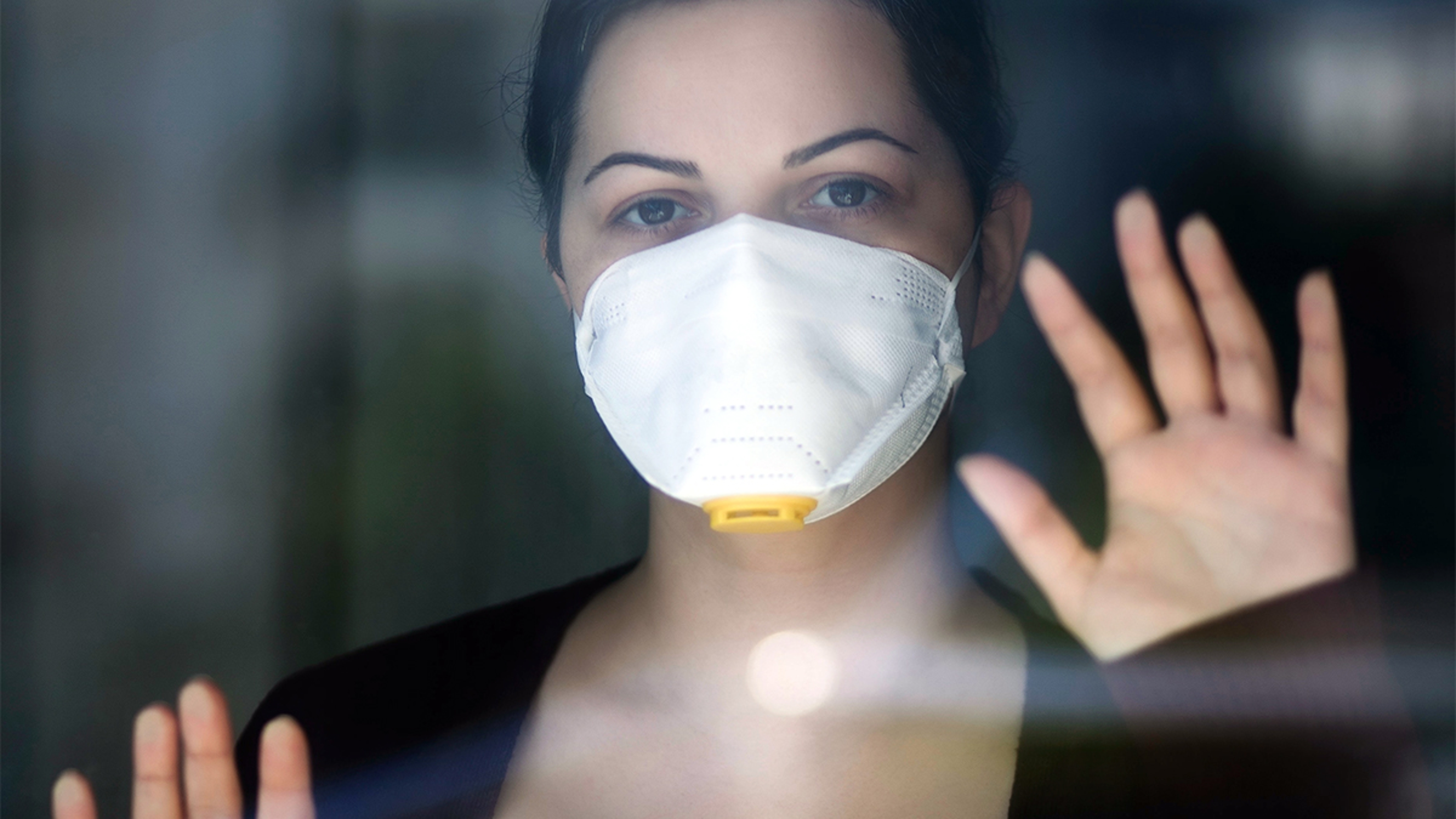 Women wearing mask against glass looking out a window