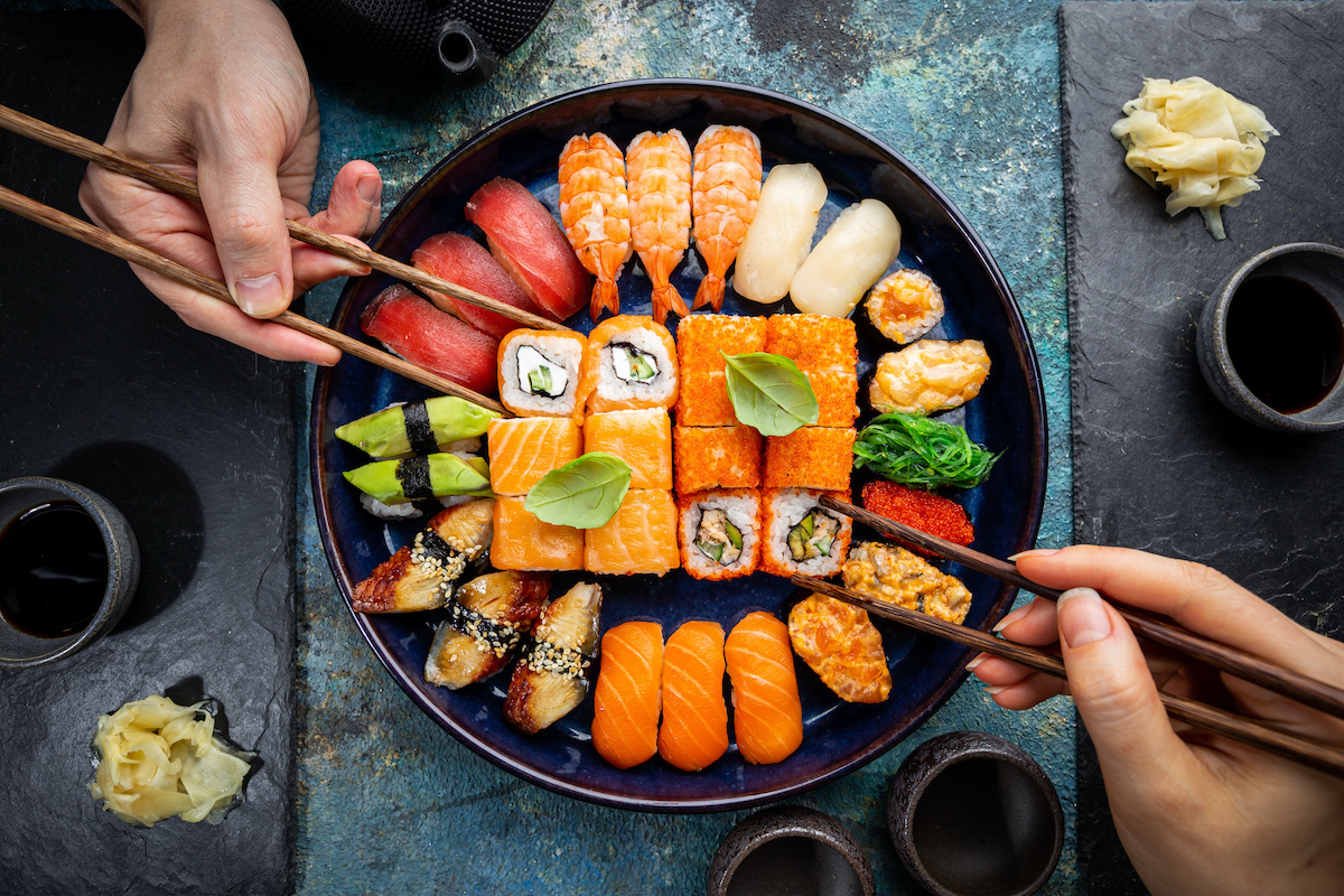 Article Cards Featured Image Set of sushi and maki with soy sauce with human hands over blue background. Top view with copy space