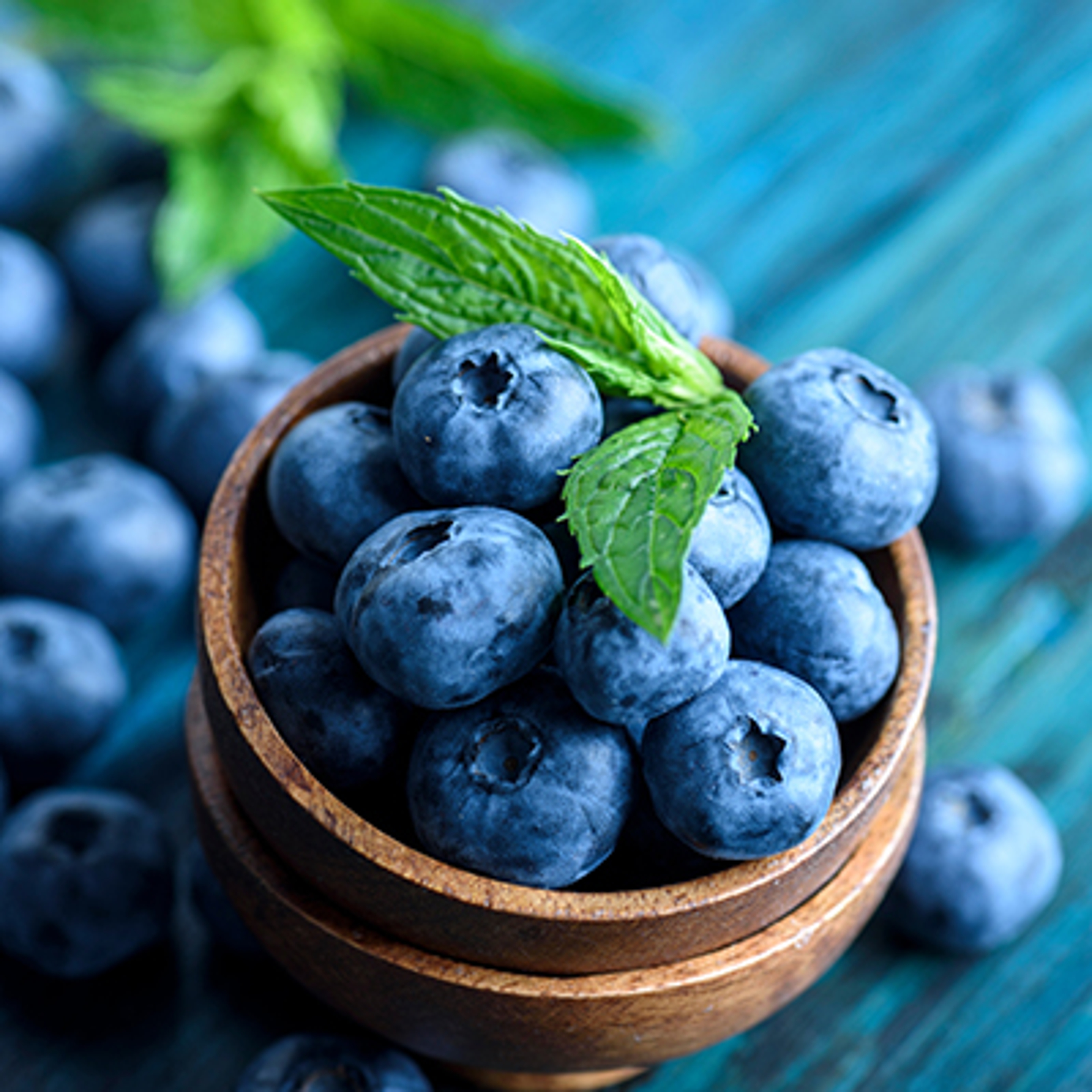 Bowl of fresh blueberries on blue rustic wooden table closeup.