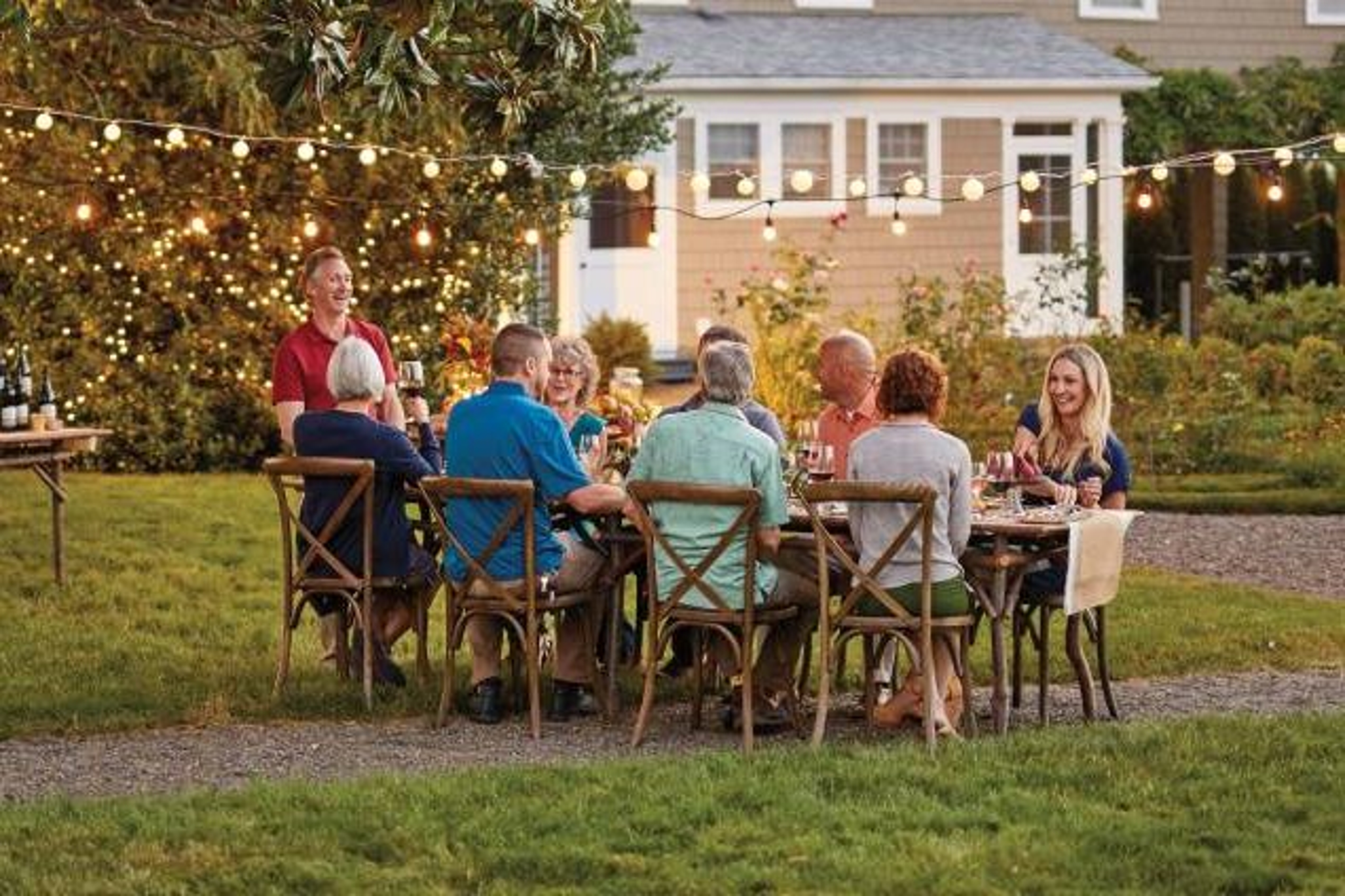 backyard party with people enjoying a meal at a farm table under a tree.