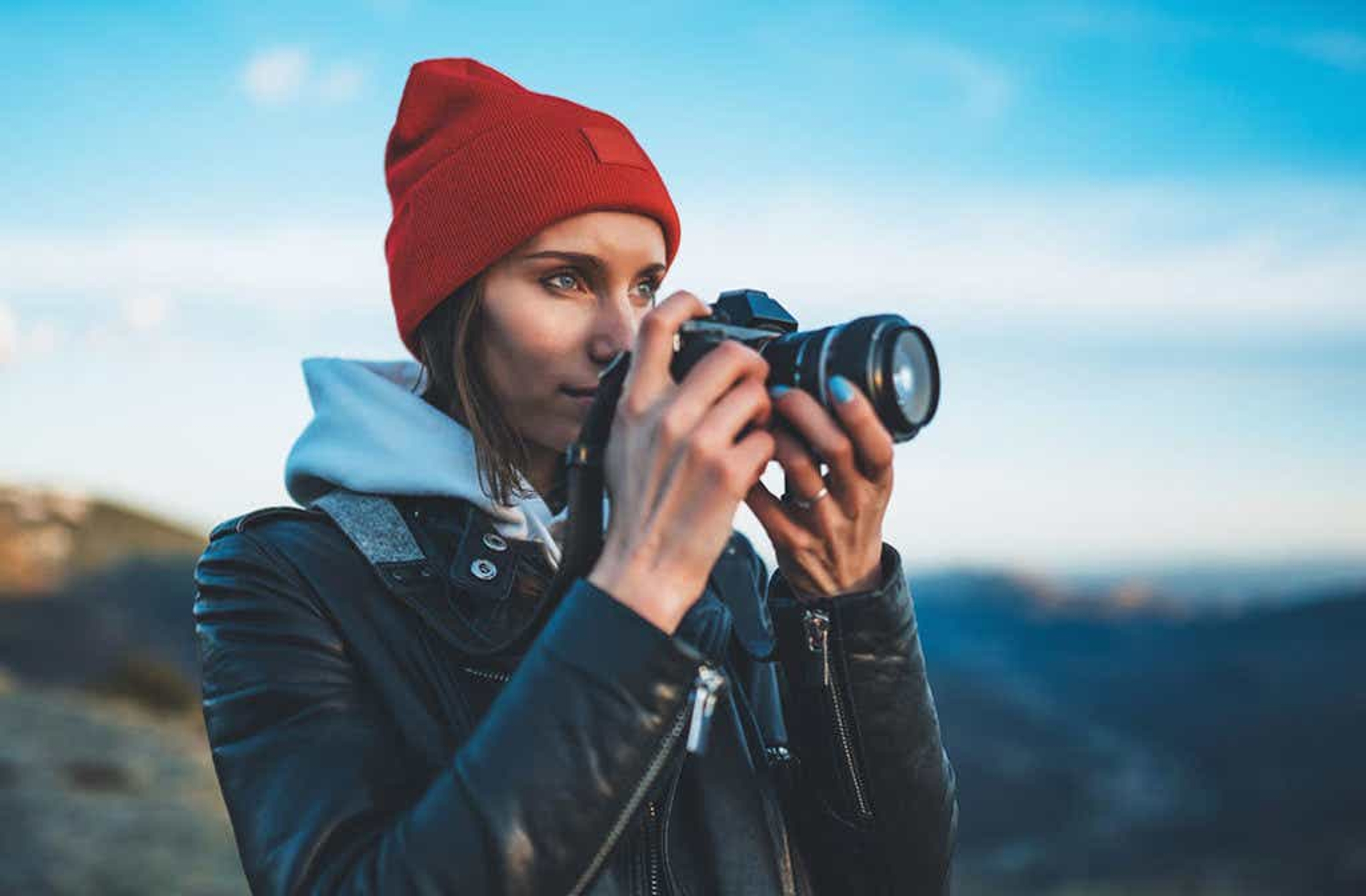 Women outdoors wearing a jacket and beanie hat holding a camera