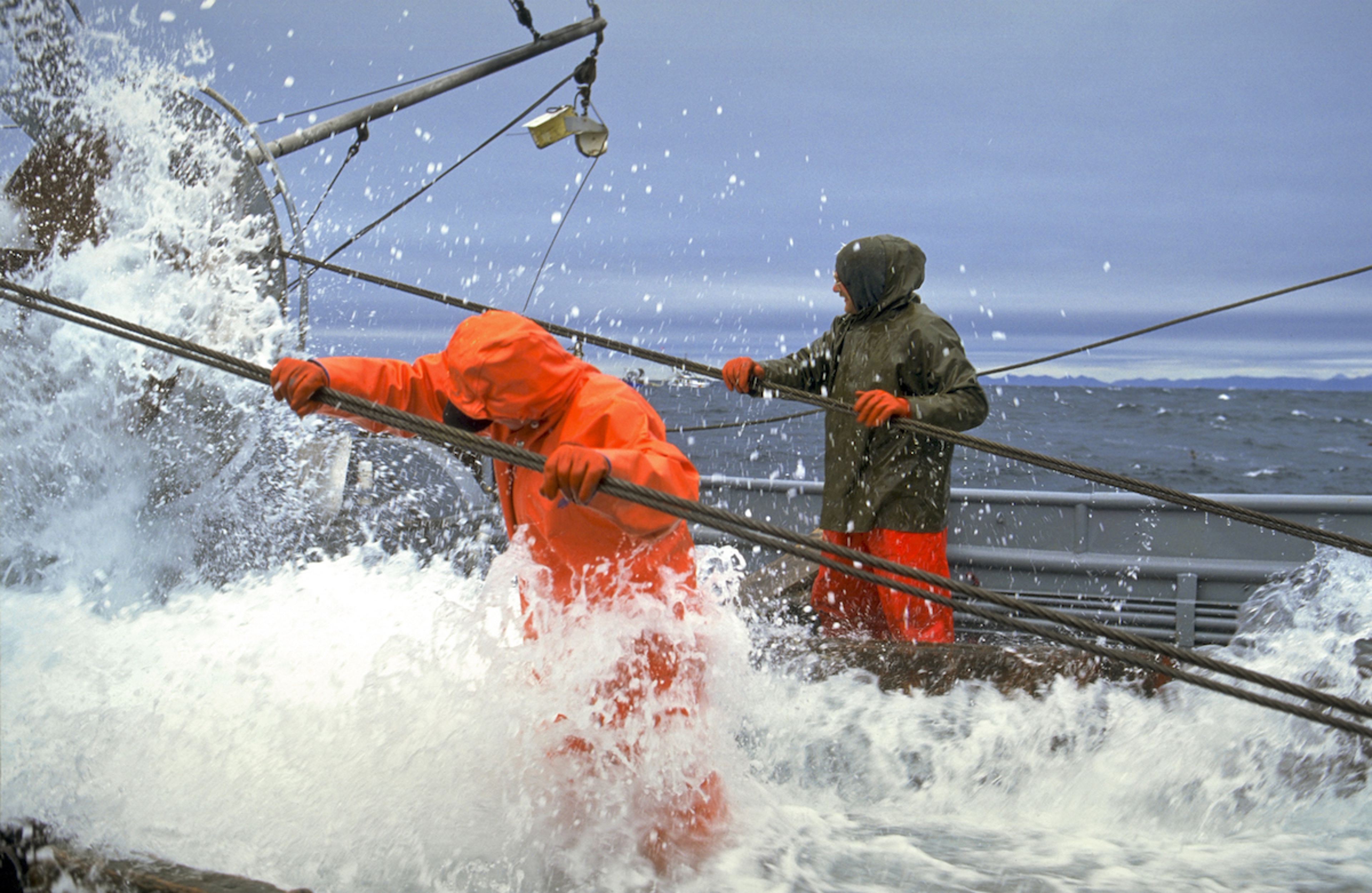 Article Cards Featured Image Alaska. Commercial fishing boat crew members help wind in the cables on The Dawn trawler during a Pollock opener out of Kodiak. Rough seas.