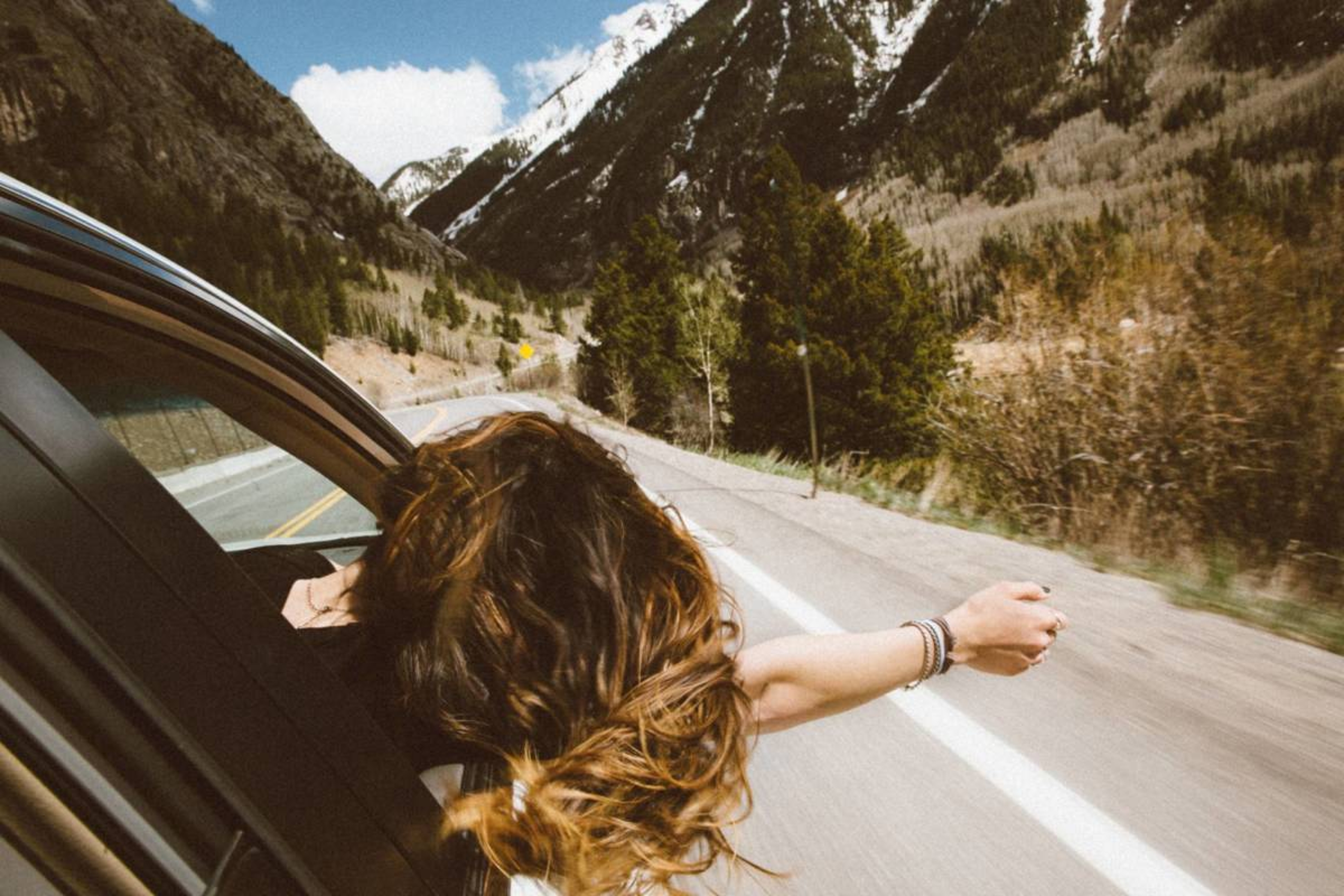 Women with head and arm sticking out of a car window while going down a highway on a road trip