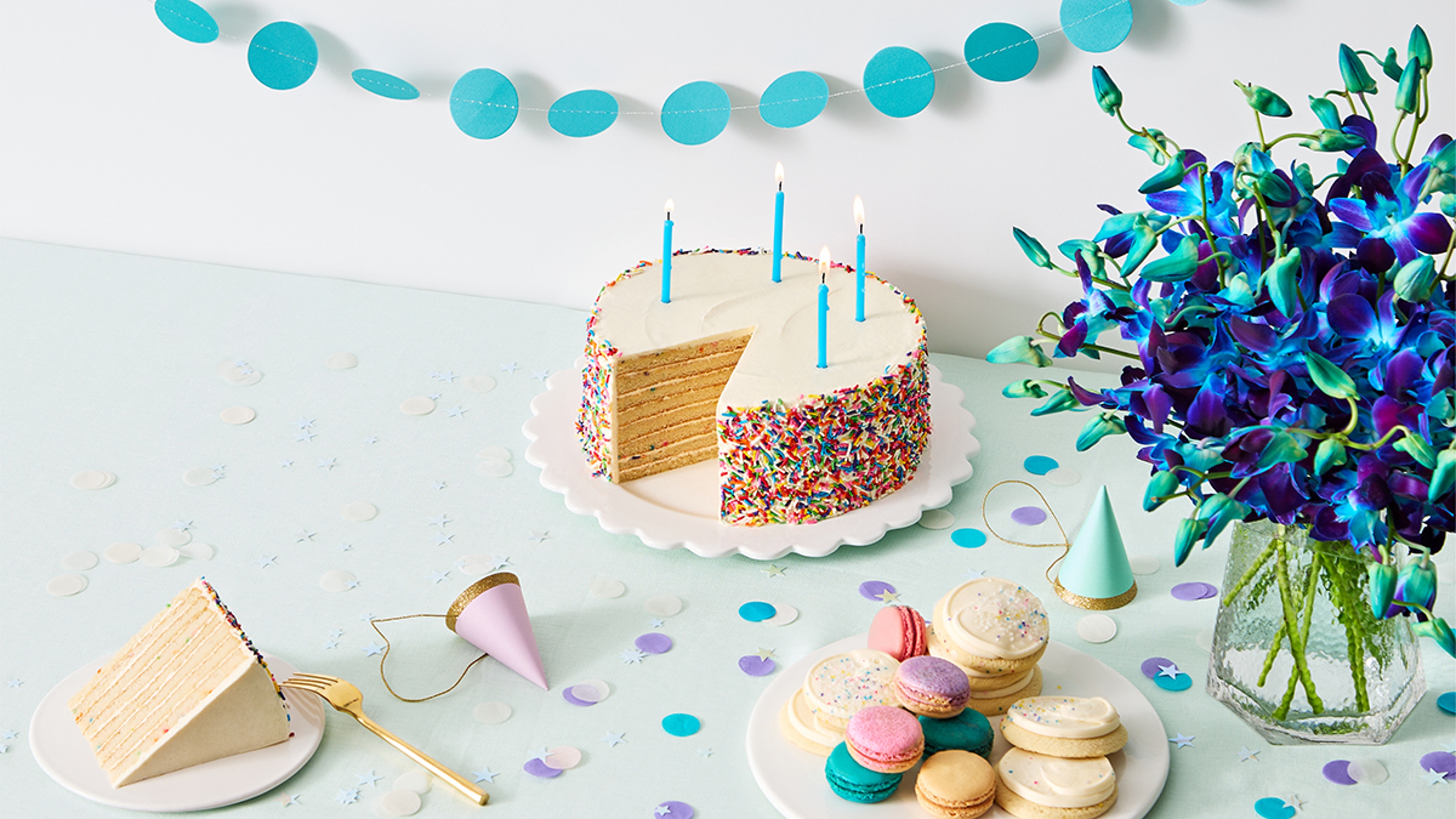 Birthday cake surrounded by cookies, flowers, and presents.