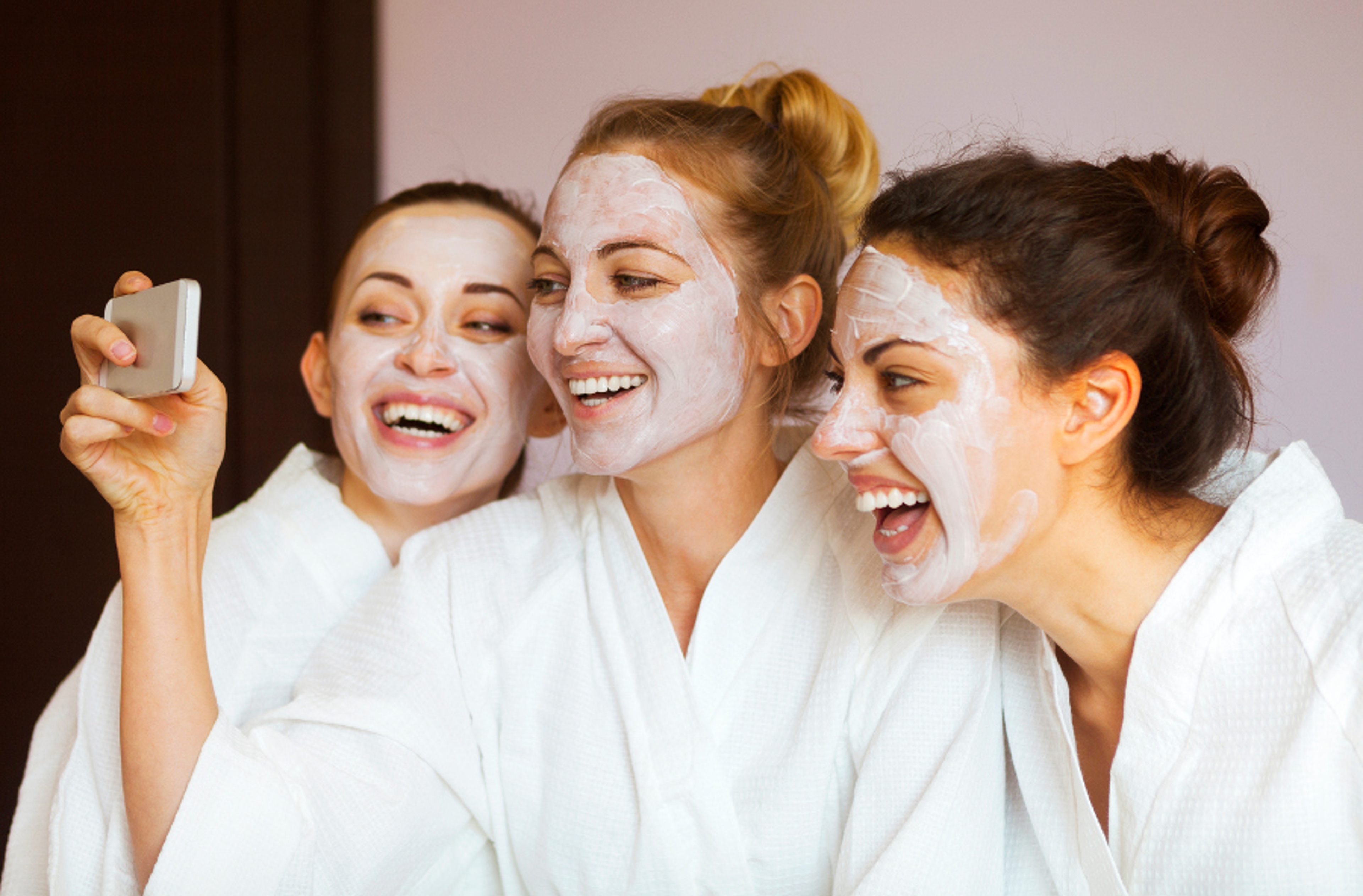 Article Cards Featured Image Three young happy women with face masks taking selfi at spa resort. Frenship and wellbeing concept