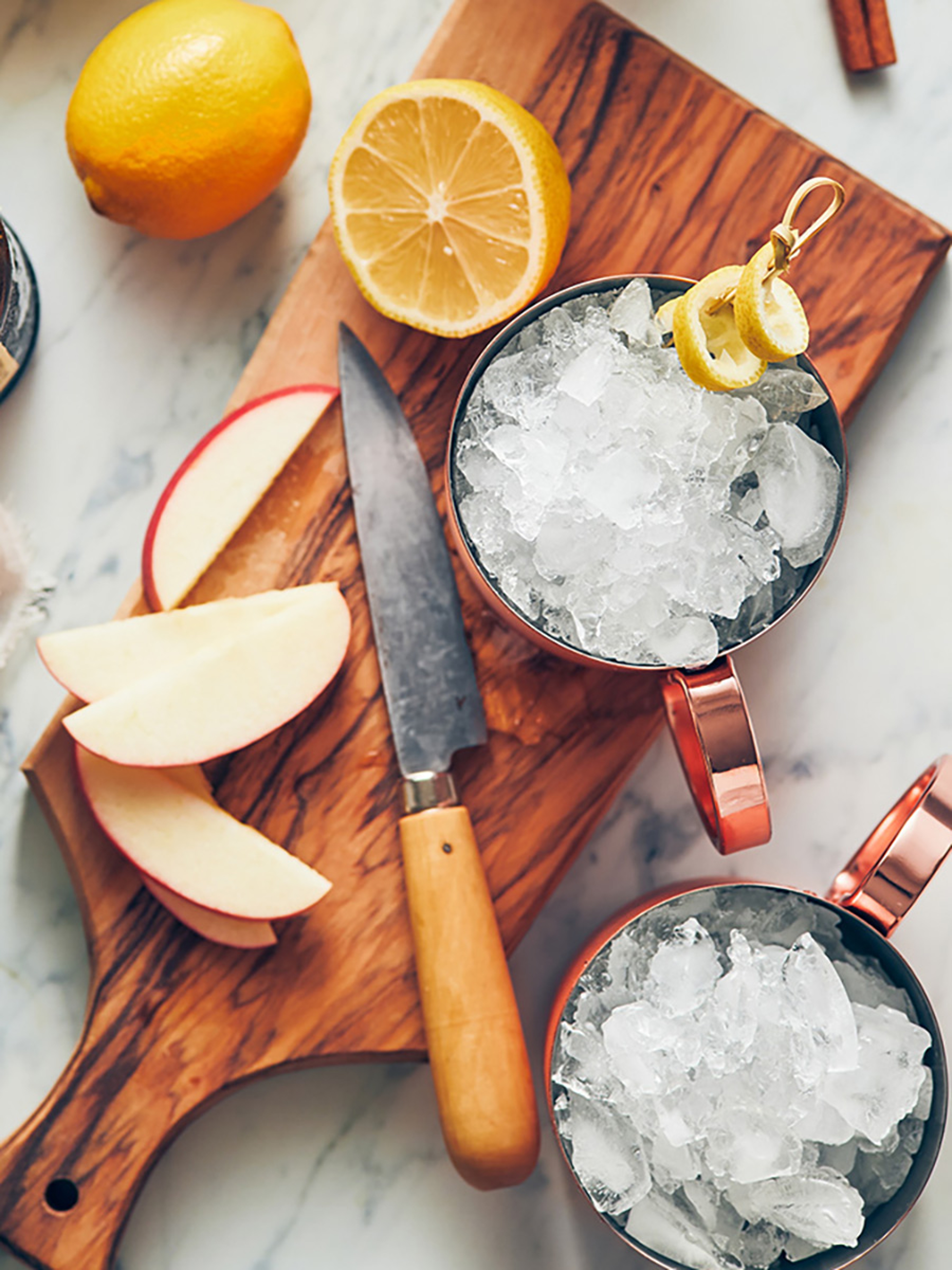 Two copper cups full of ice for Moscow Mules on a wooden cutting board.