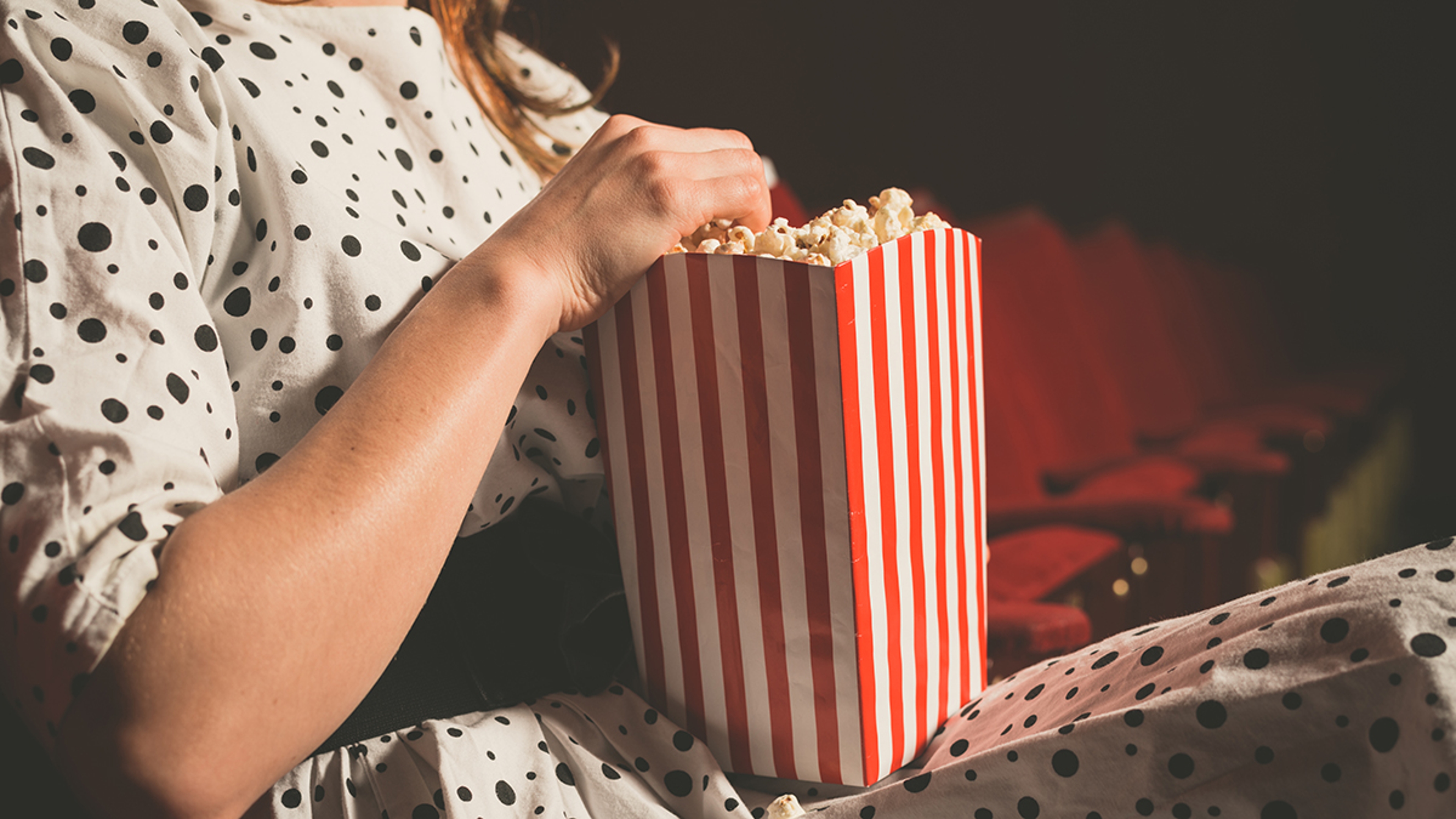 Woman holding a box of popcorn while sitting in a cinema.