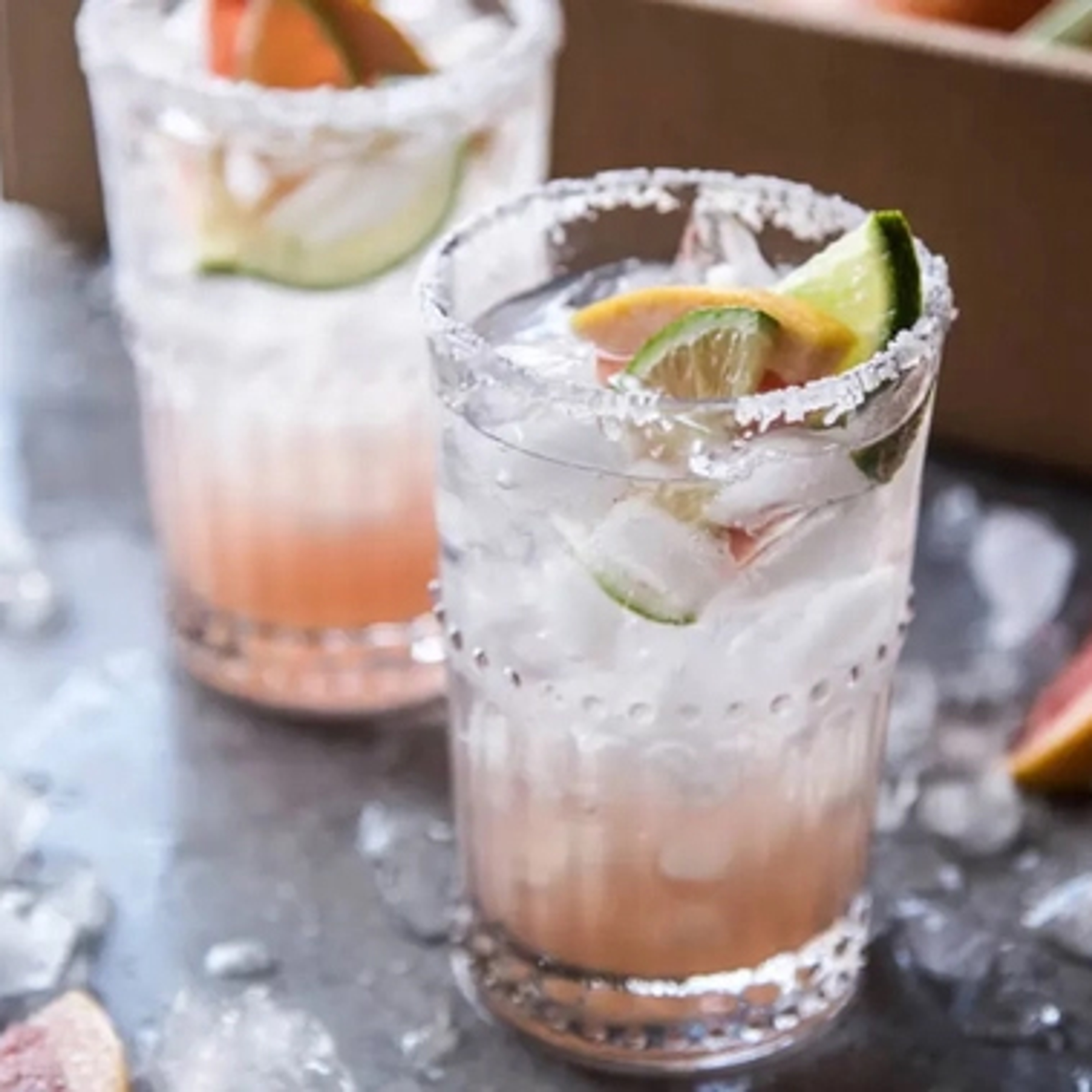 Two grapefruit palomas in glasses with slices of lime.