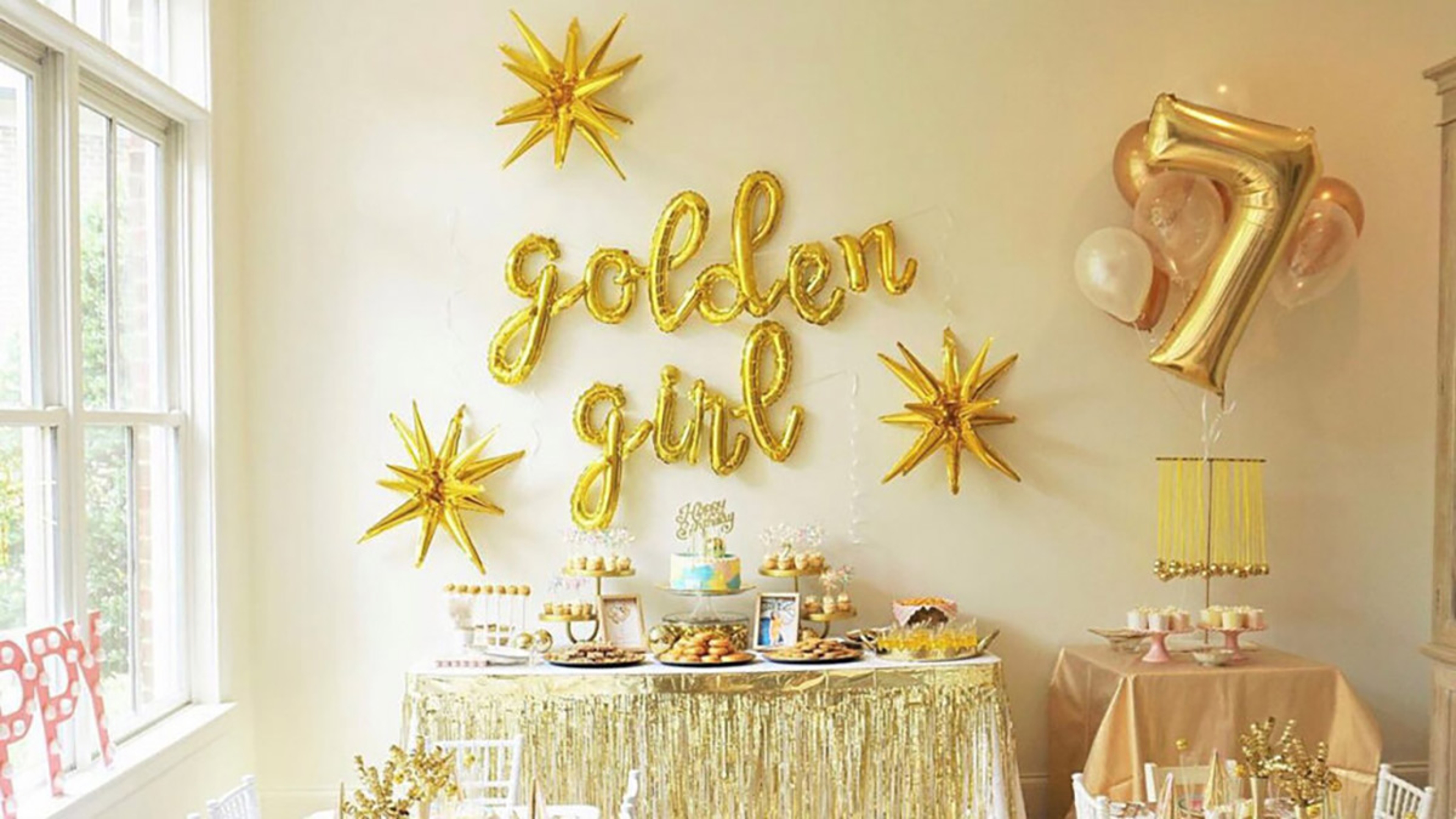 Golden birthday balloons above a table of food.