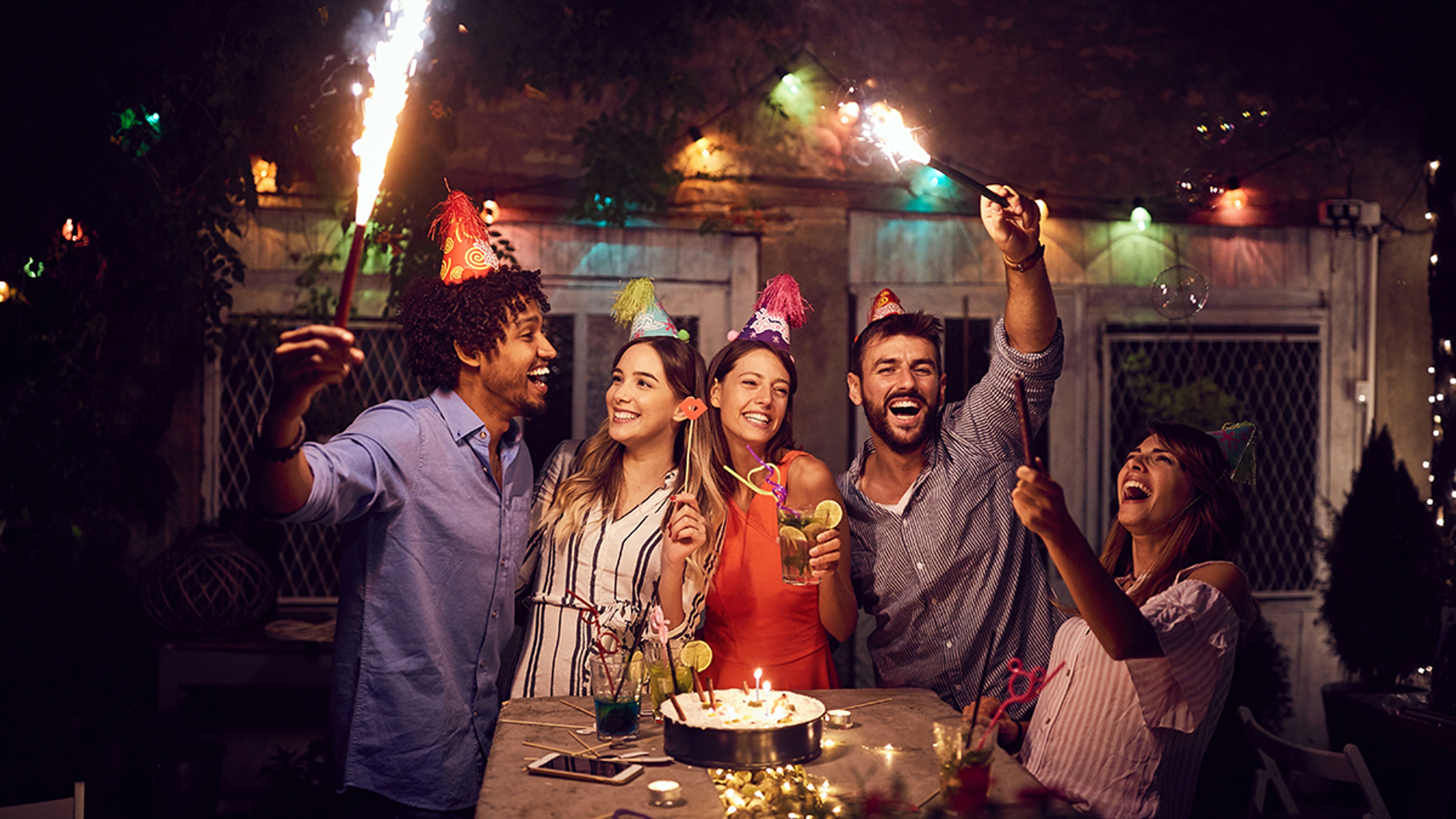 Cheerful group of young friends having birthday party in the club with cake and candles at night. Party, fun, birthday concept.